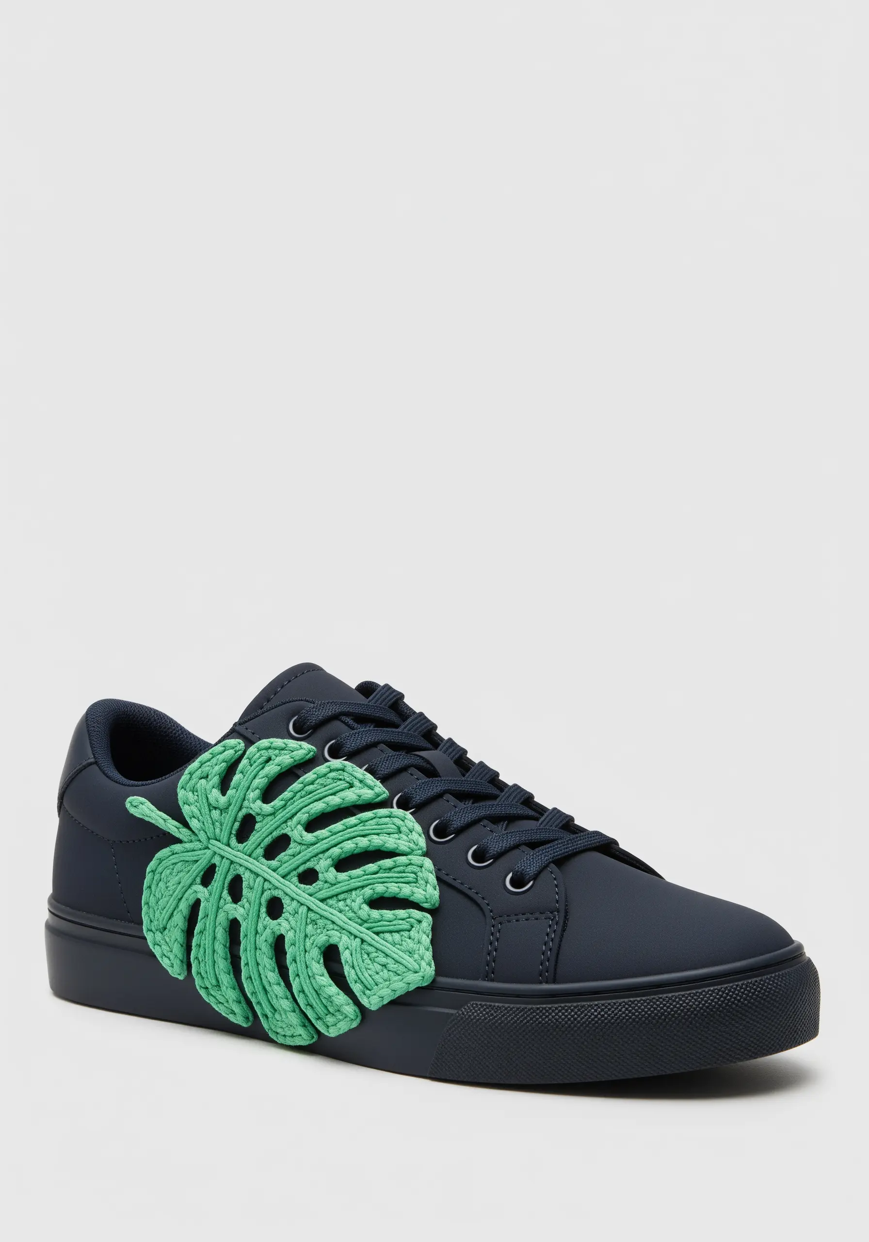 A large, three-dimensional green crochet monstera leaf attached to a navy blue sneaker.