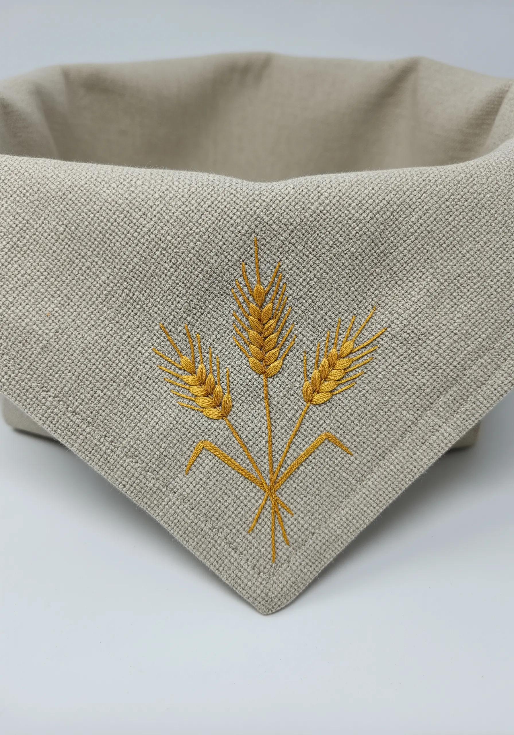 Three stalks of wheat embroidered in golden thread on the corner of a linen basket.