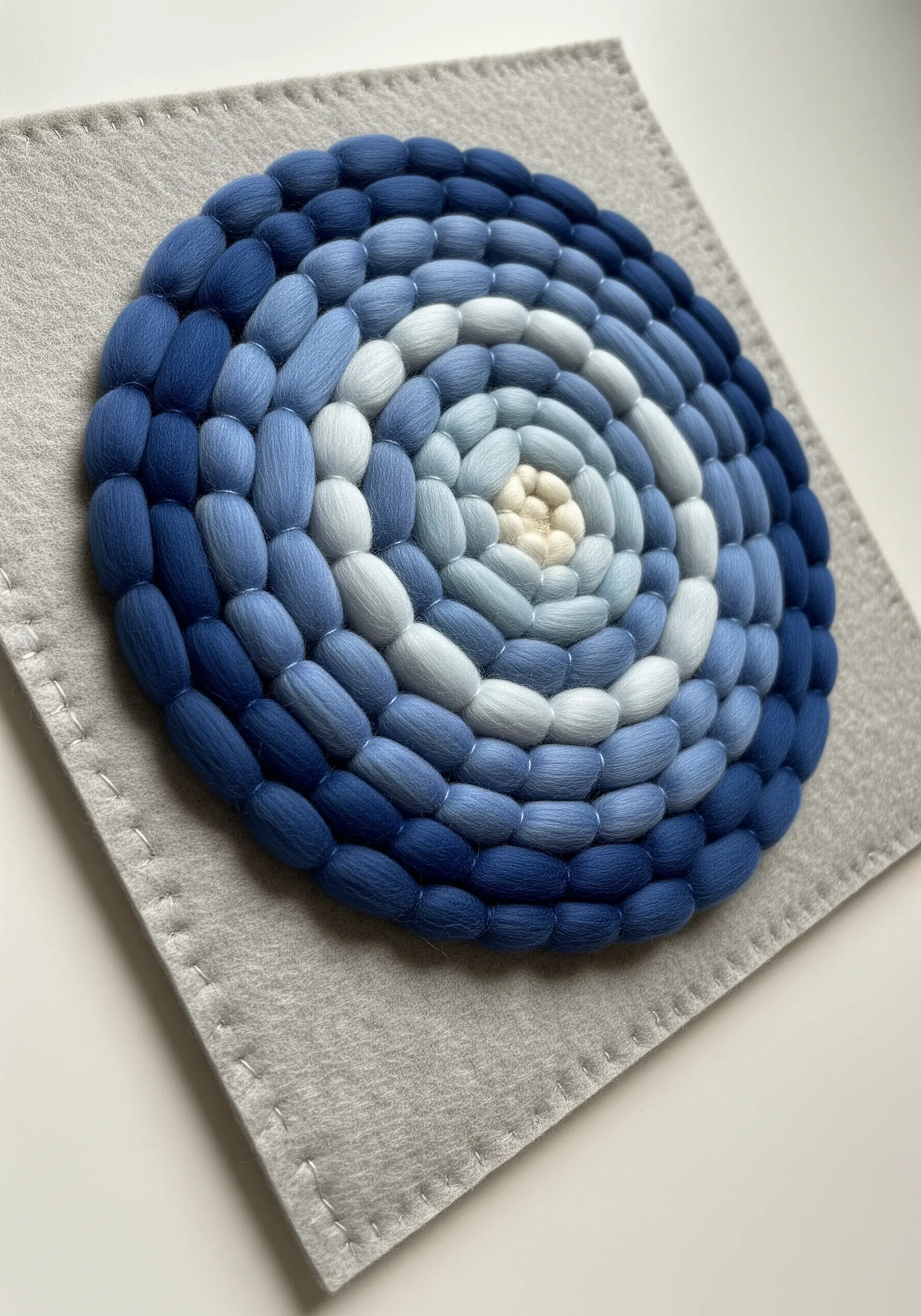 A spiral of coiled wool roving in shades of blue, from dark to light.