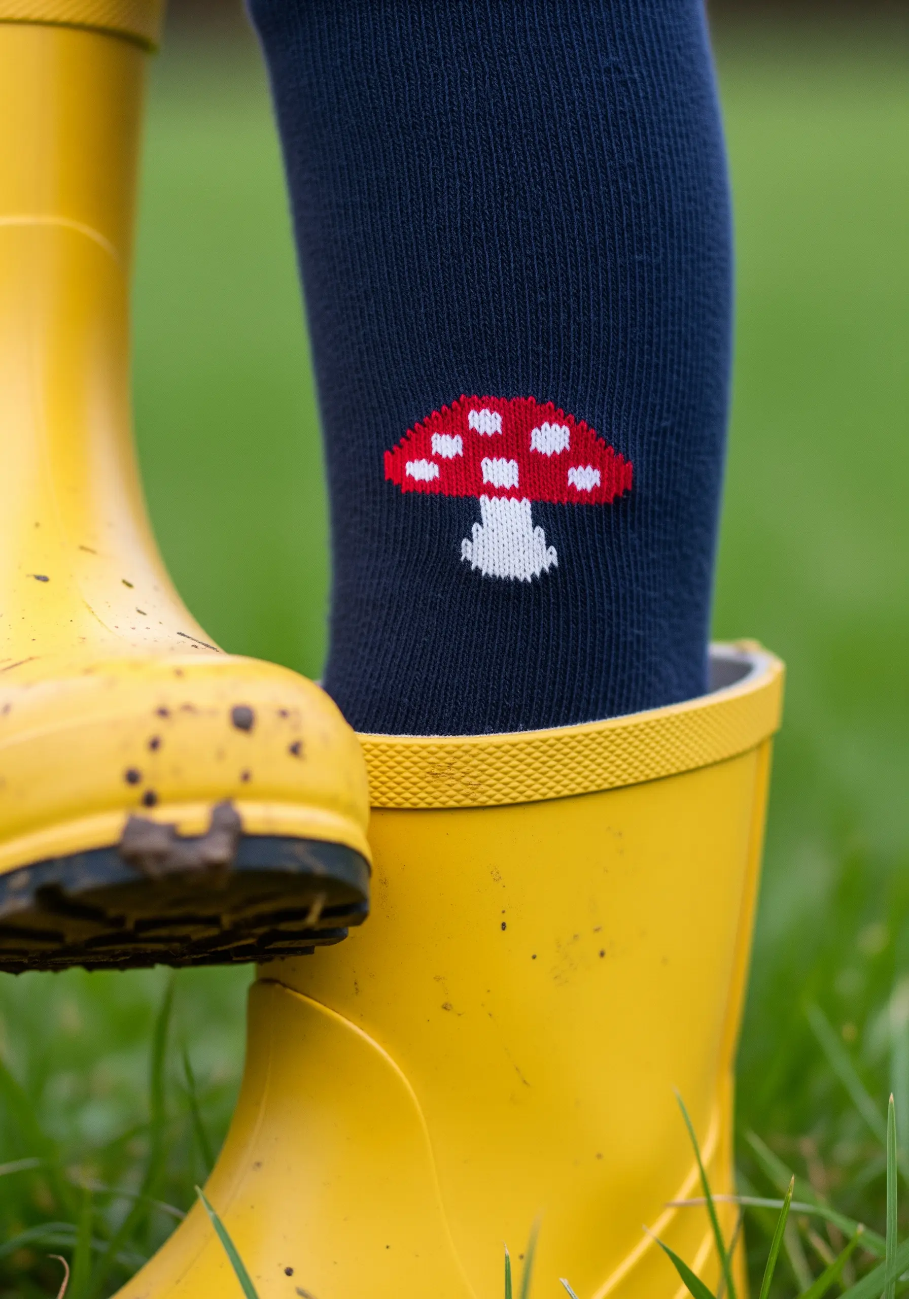 A pixelated-style red and white mushroom embroidered on a dark blue sock near yellow rain boots.