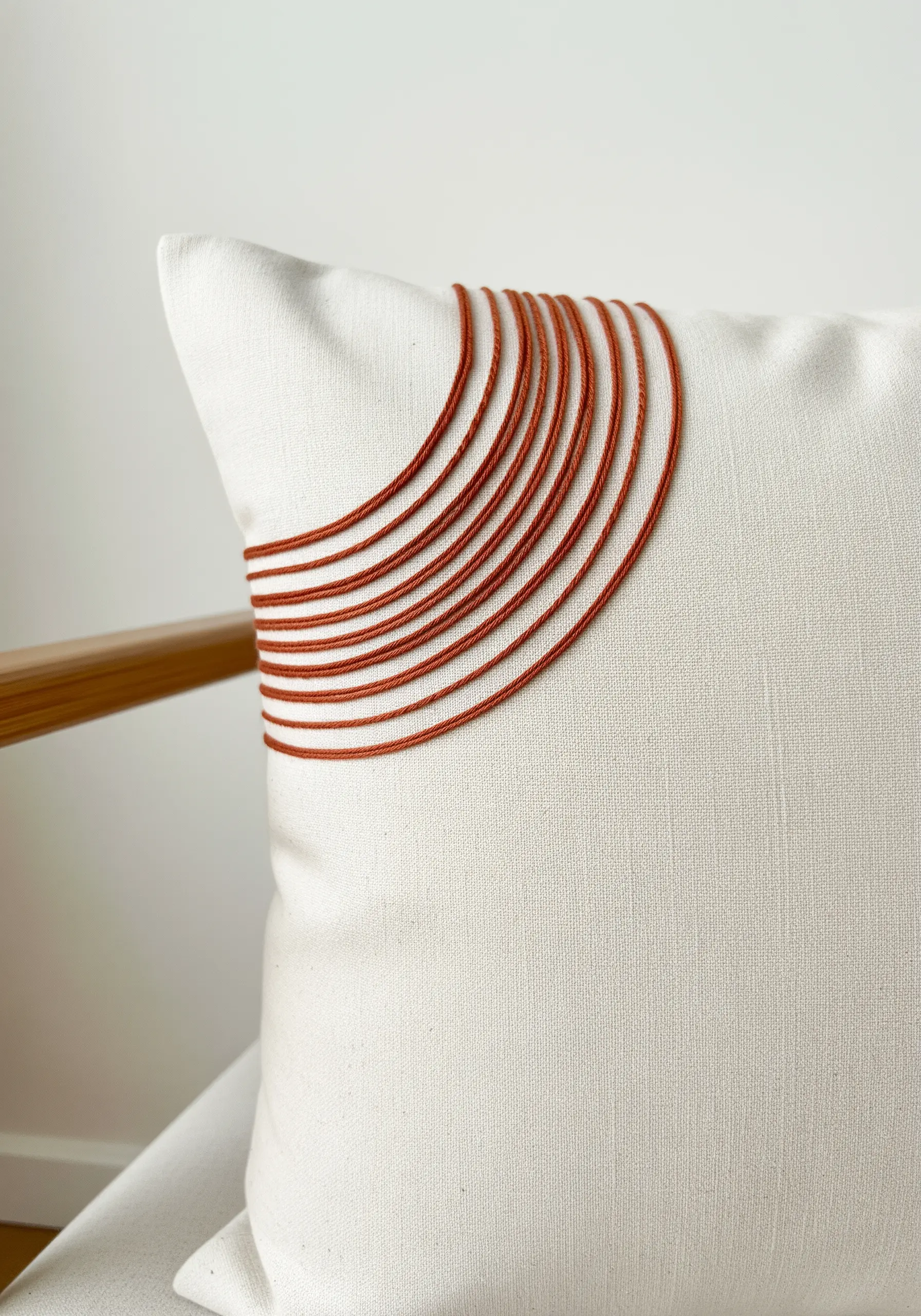 Burnt orange thread forming concentric arcs on the corner of a white linen pillow.