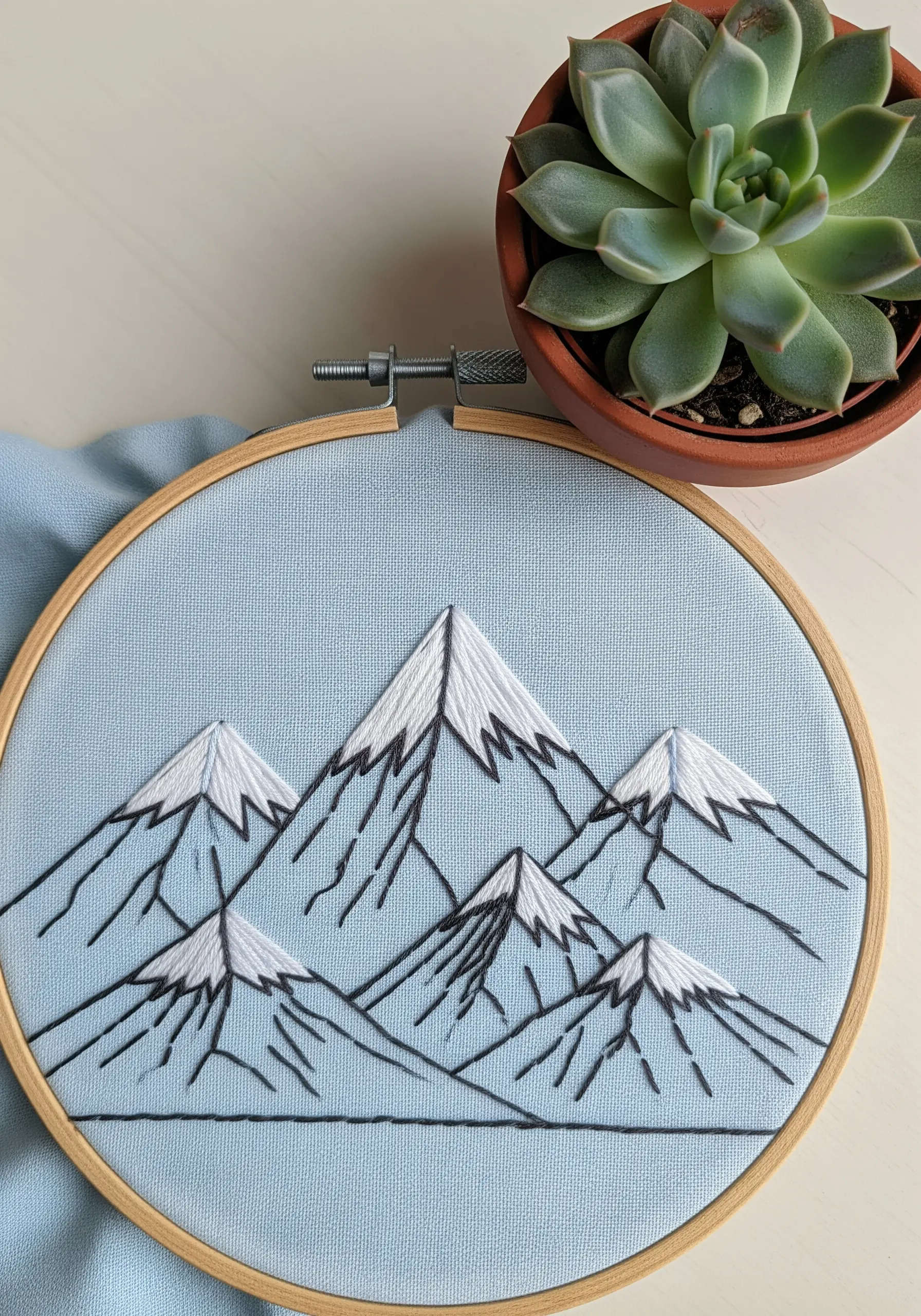 A graphic mountain range with black line art and white satin stitch snow caps.