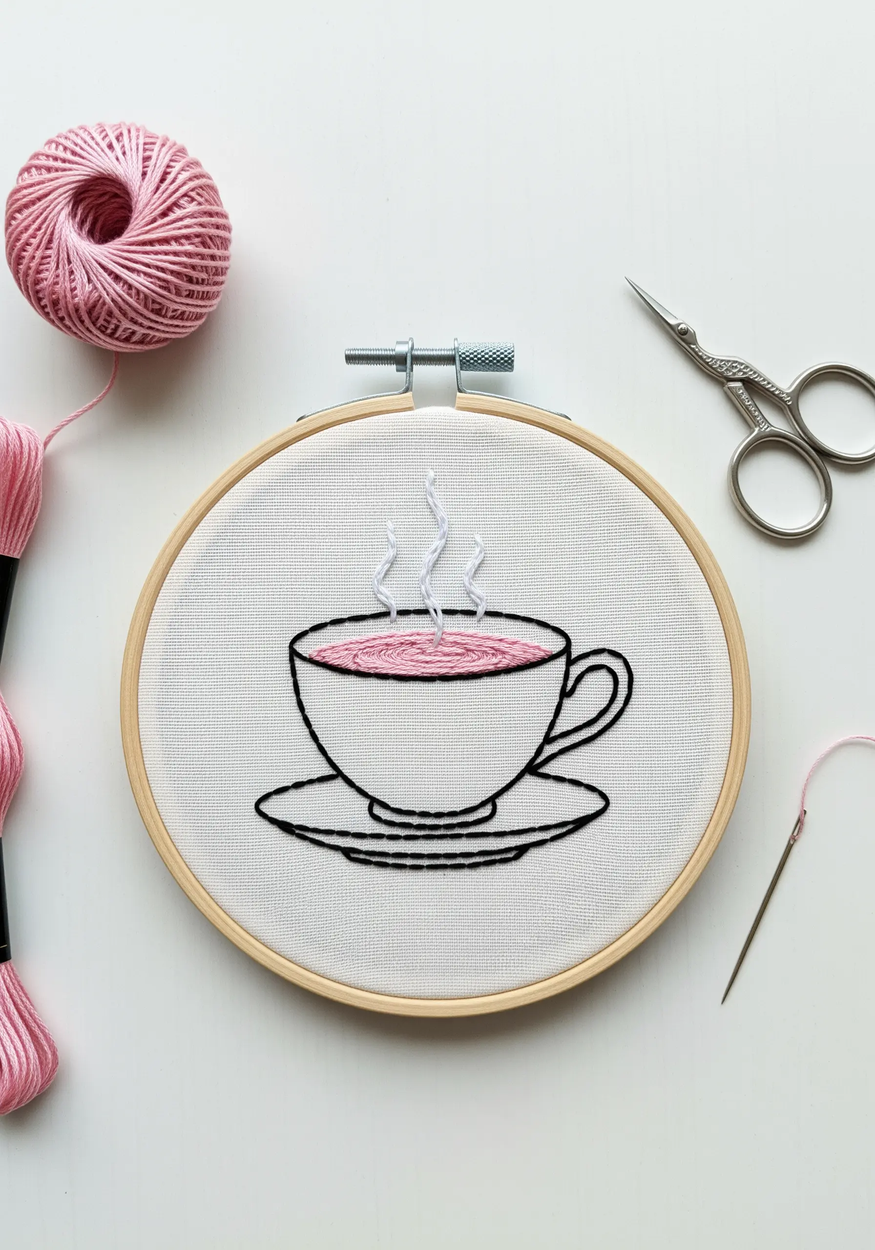 Line art embroidery of a tea cup, with the liquid filled in with pink satin stitch.