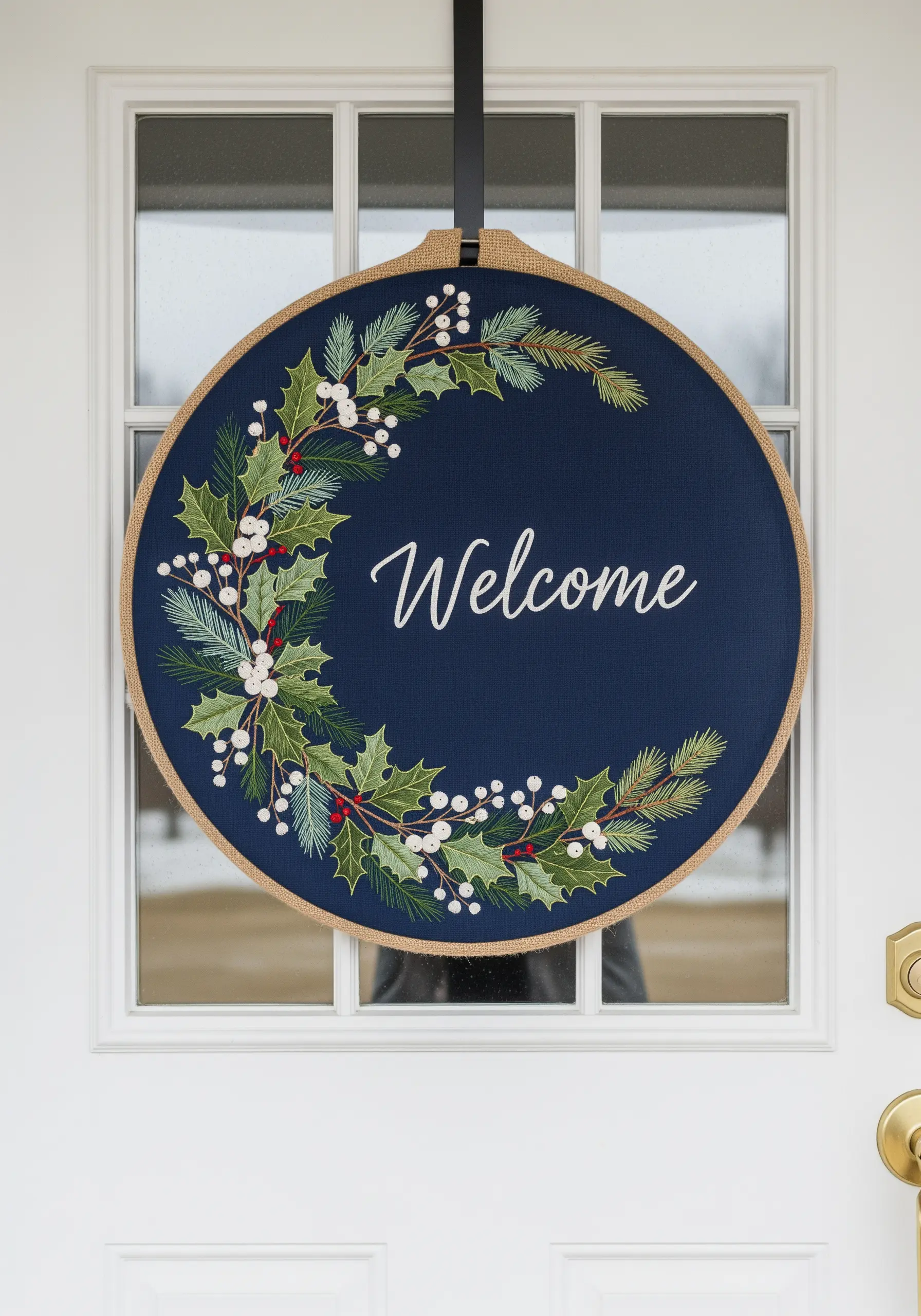 A large embroidery hoop on a front door, with a 'Welcome' message inside a holly wreath.