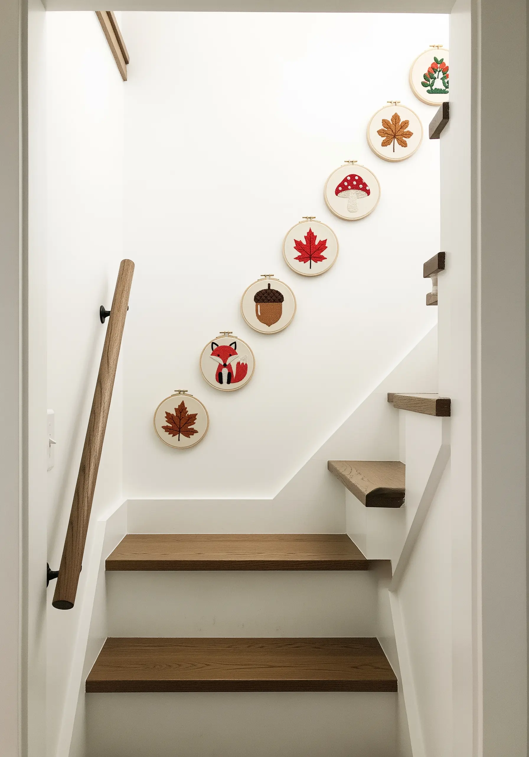 A series of small, autumn-themed embroidery hoops arranged diagonally up a staircase wall