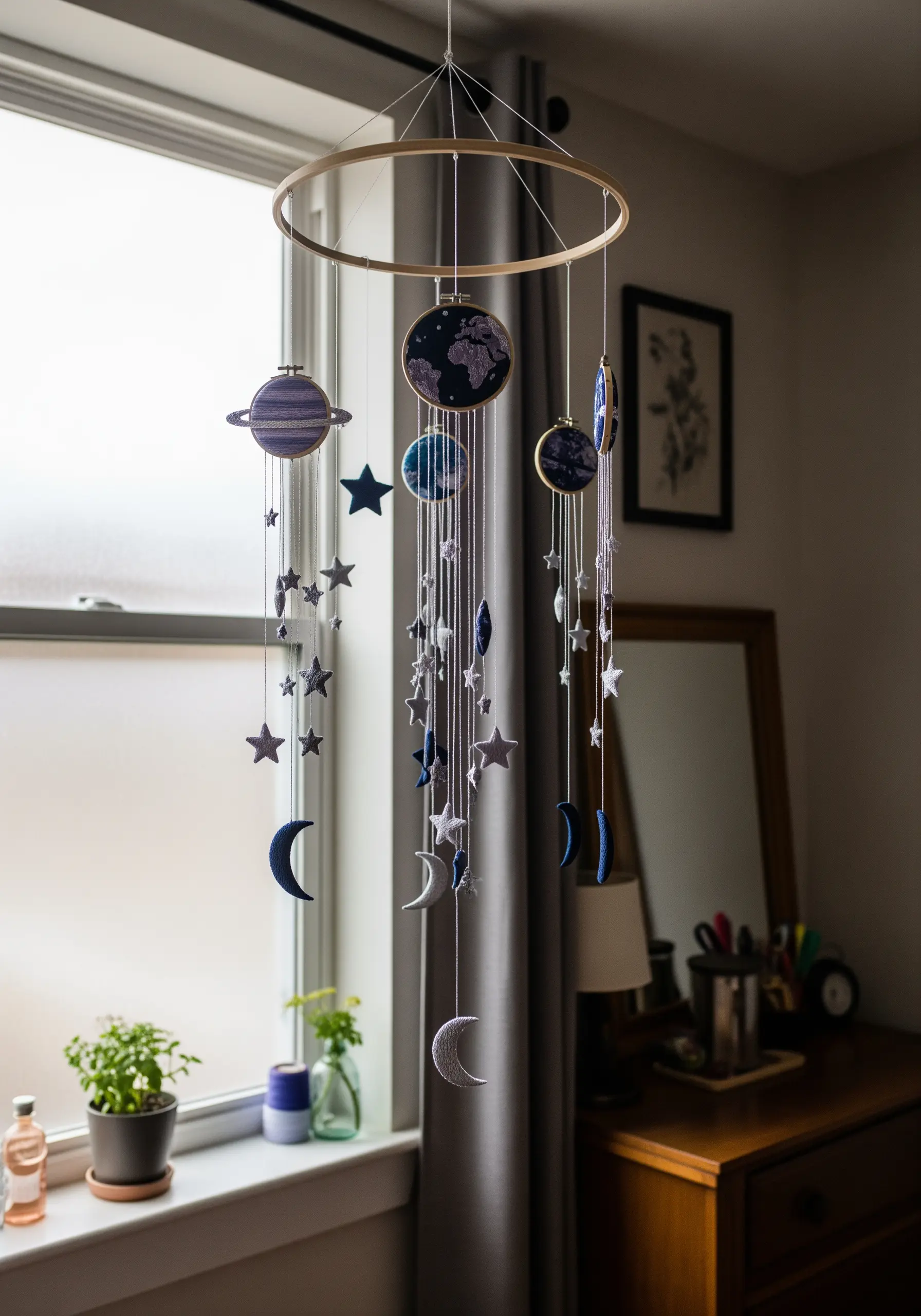 A celestial mobile with embroidered planets, stars, and moons hanging from a large hoop.