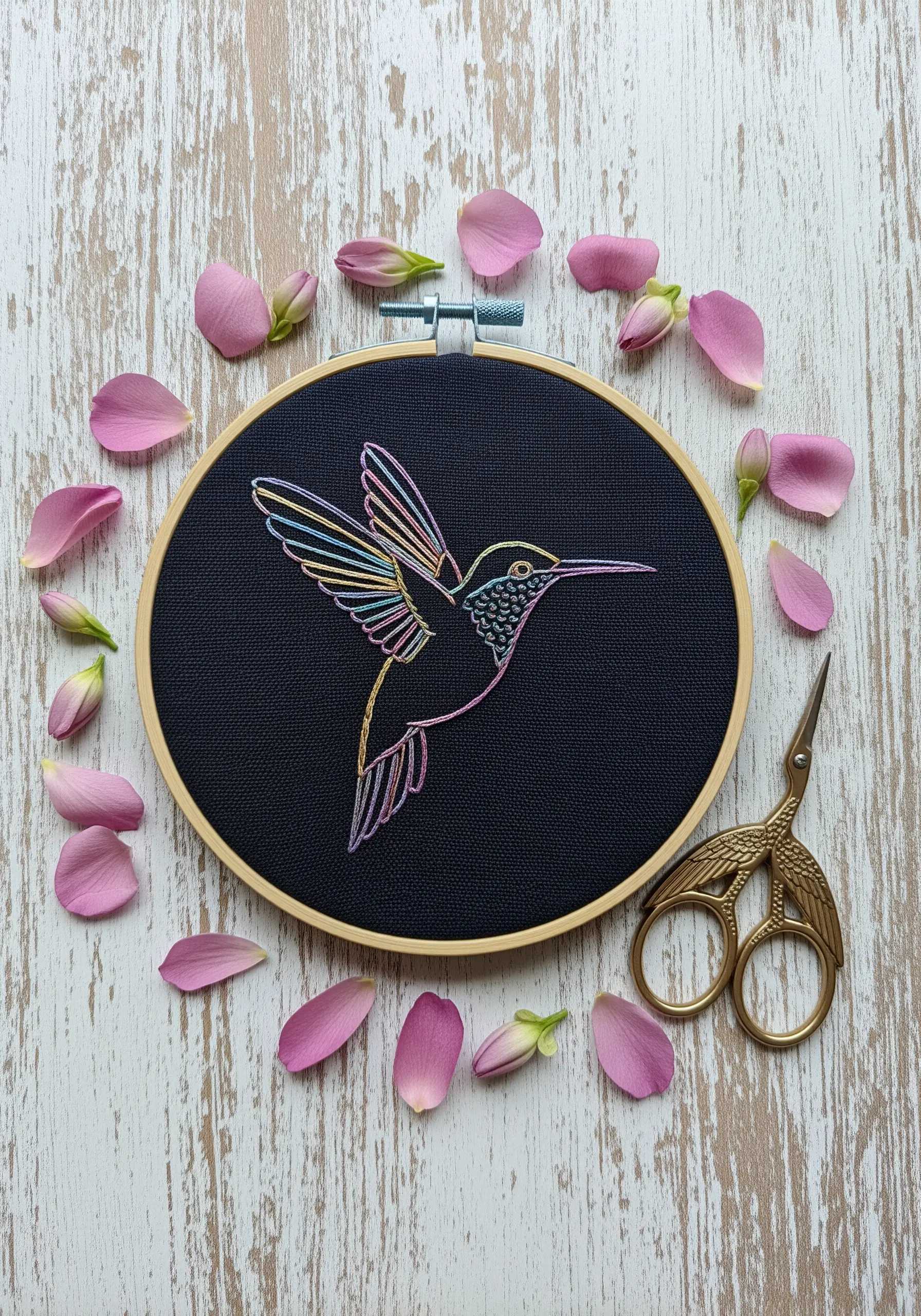 A hummingbird embroidered on black fabric using a single variegated, rainbow-colored thread.