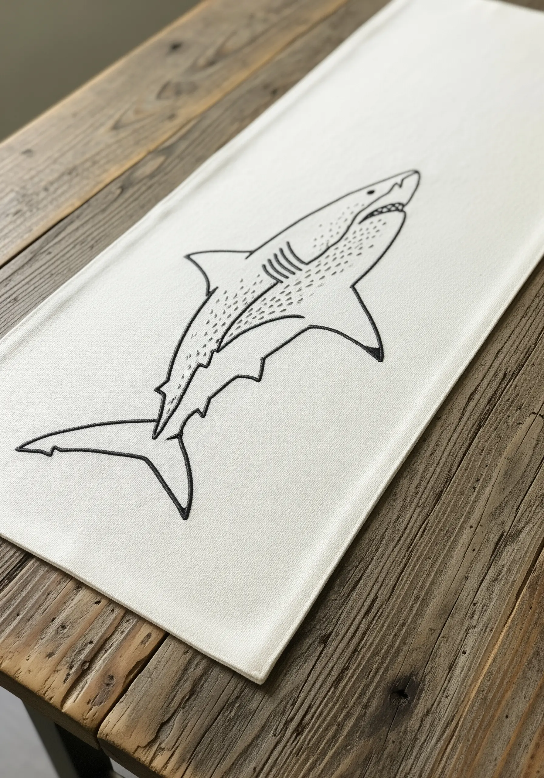 A minimalist shark embroidered in black line art on a white table runner.