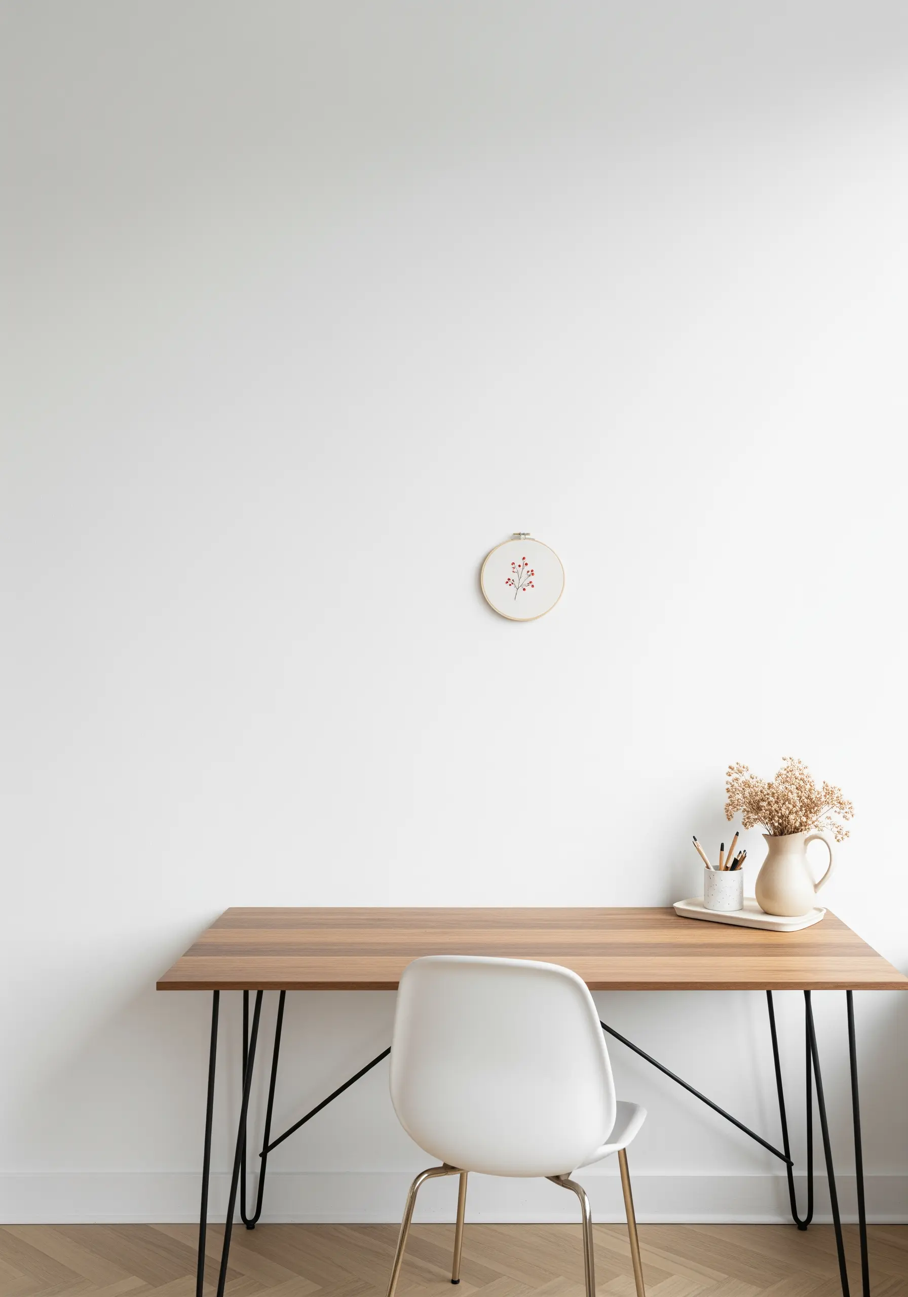 A tiny embroidery of a berry sprig in a small hoop on a large, empty white wall.