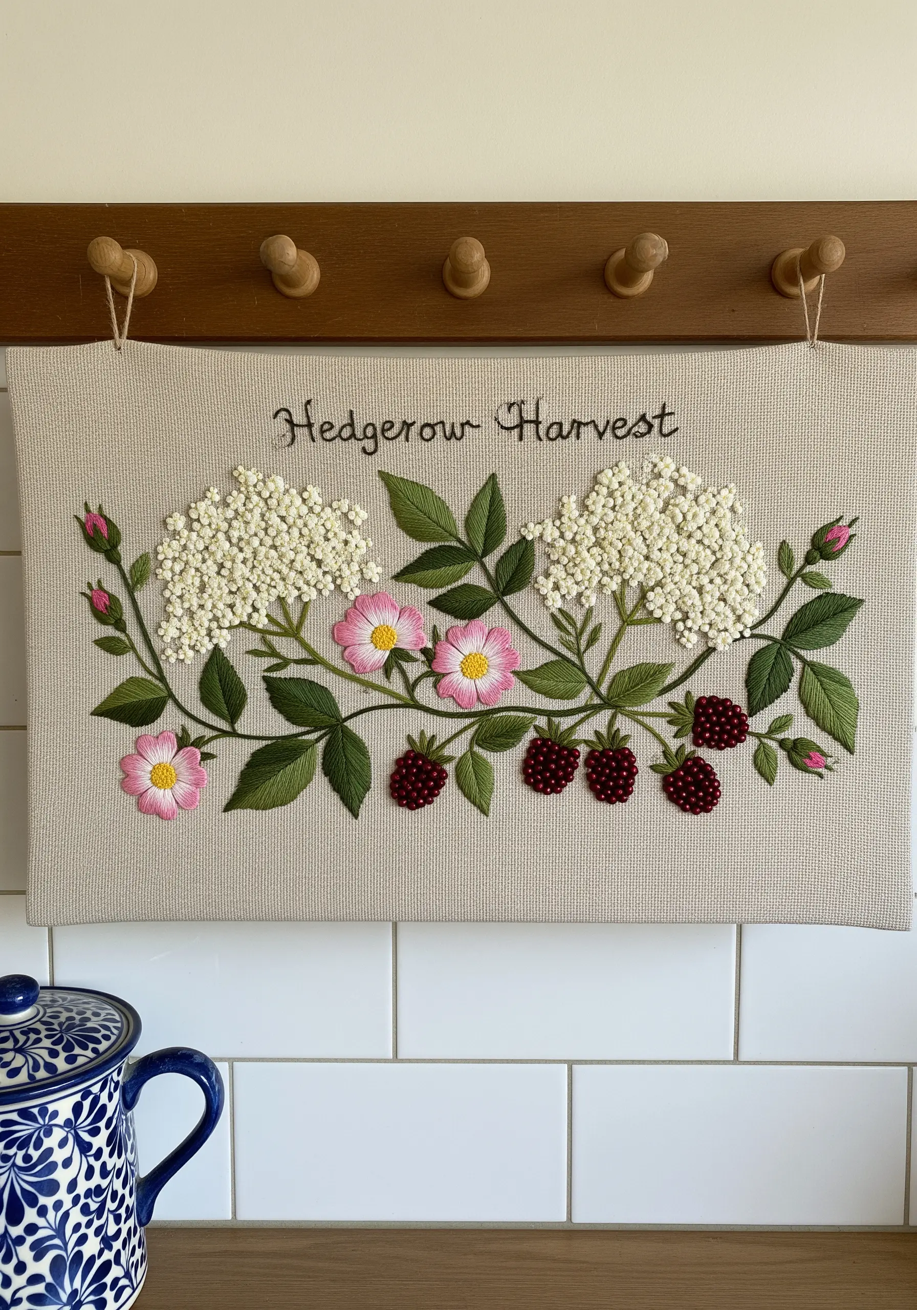 A horizontal embroidery piece featuring wild roses, elderflower, and blackberries.
