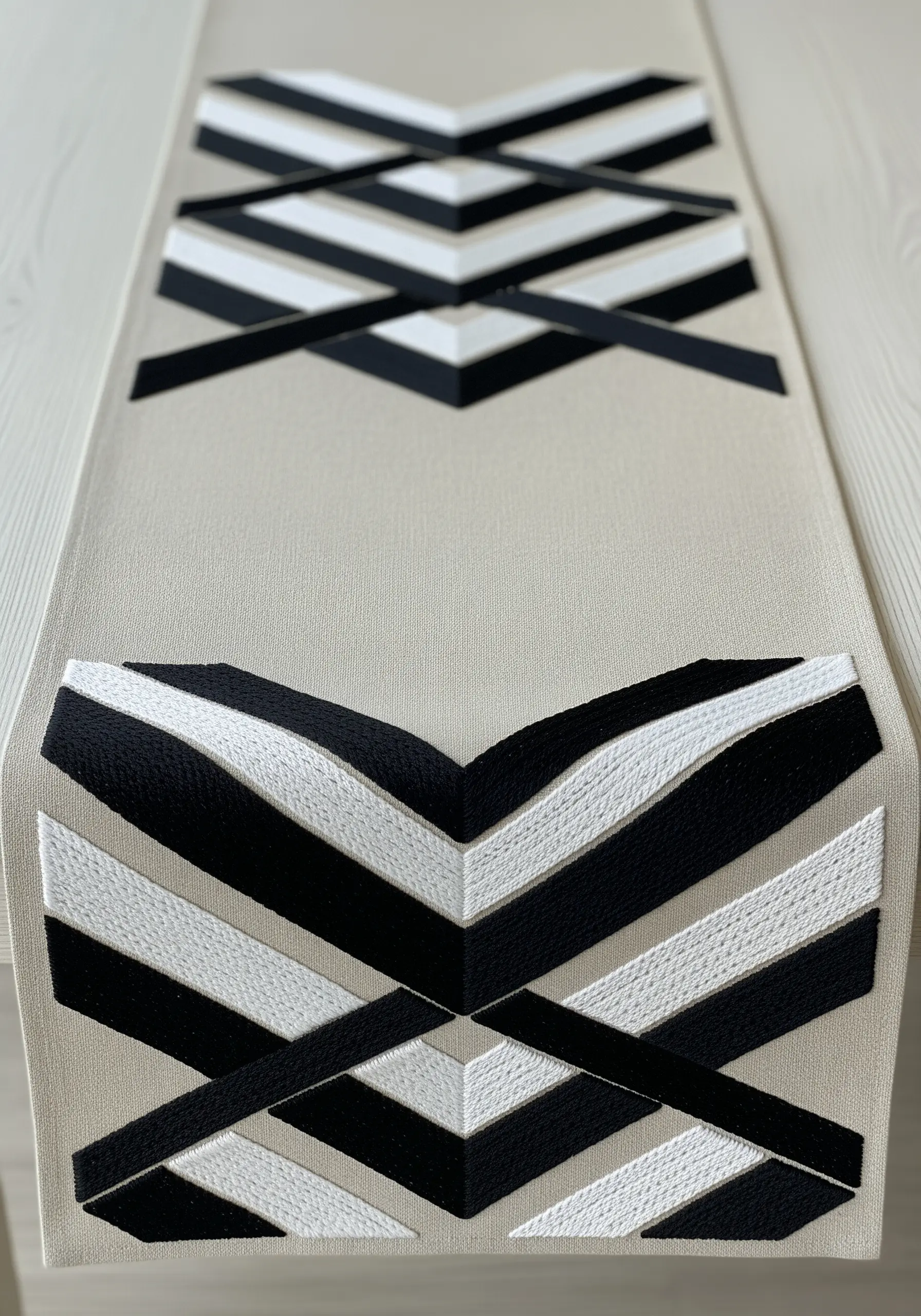 Bold black and white chevron and diamond pattern embroidered on a beige table runner.