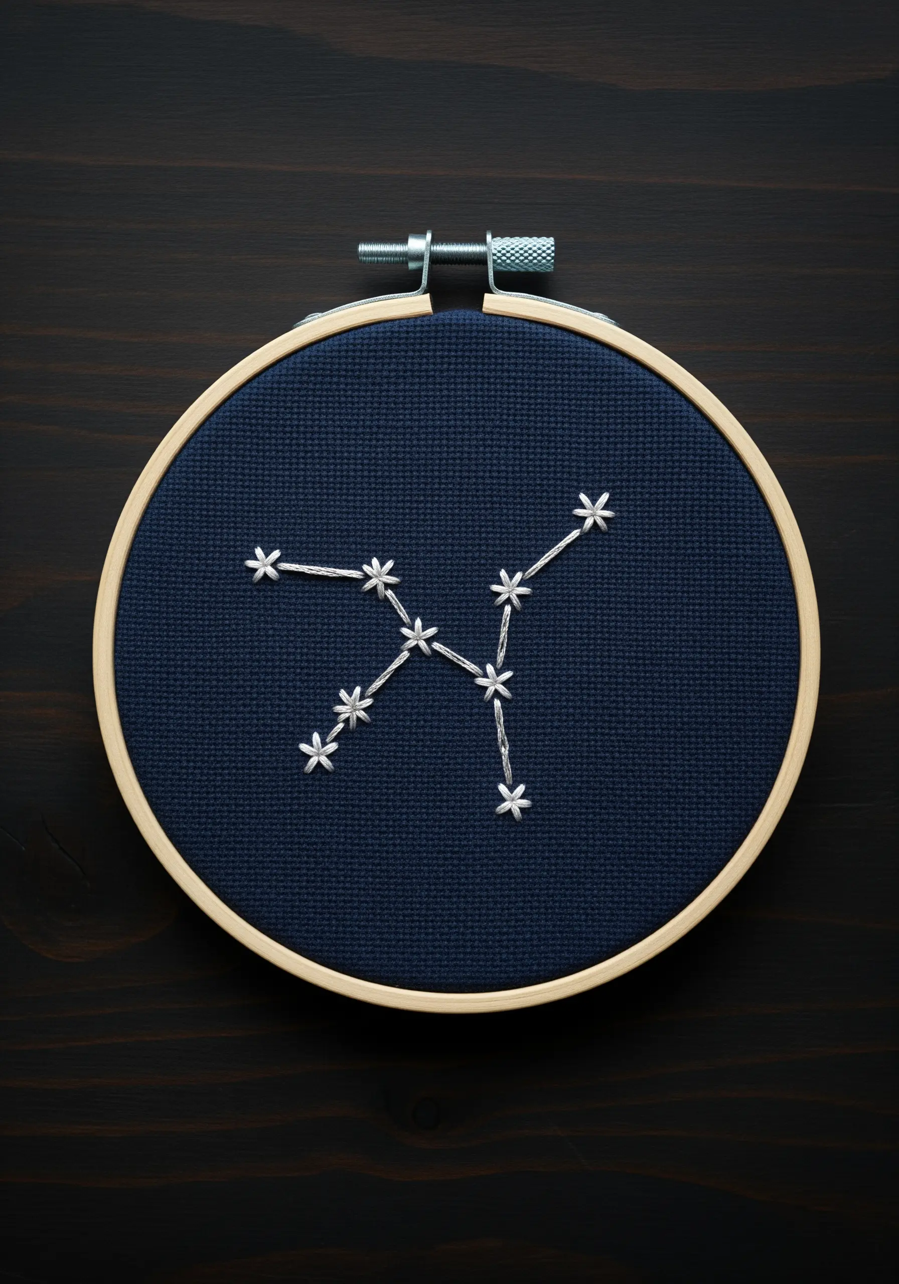 A simple constellation embroidered with white thread on dark navy fabric.