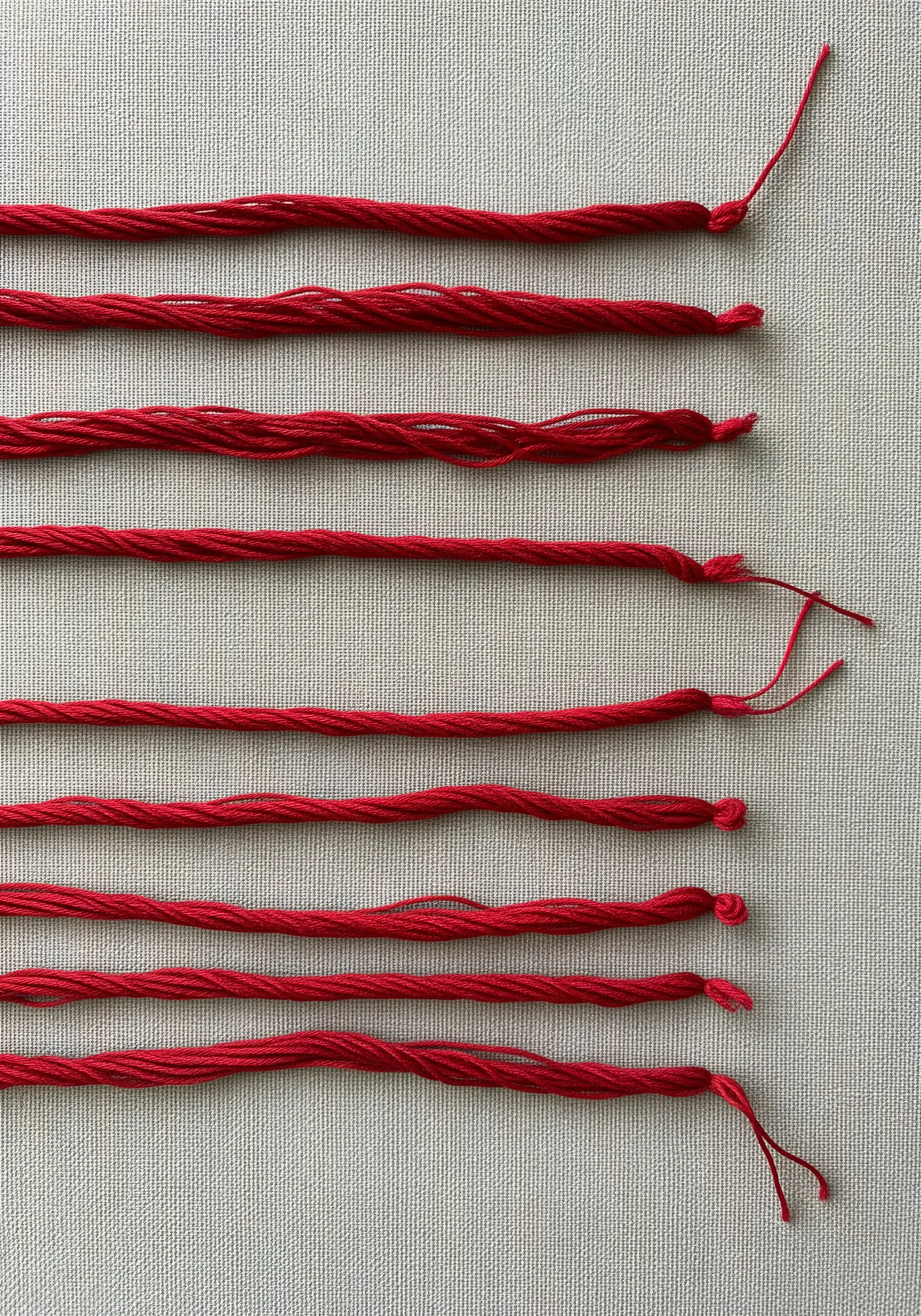 Parallel horizontal lines of thick, twisted red cord couched onto a neutral canvas.