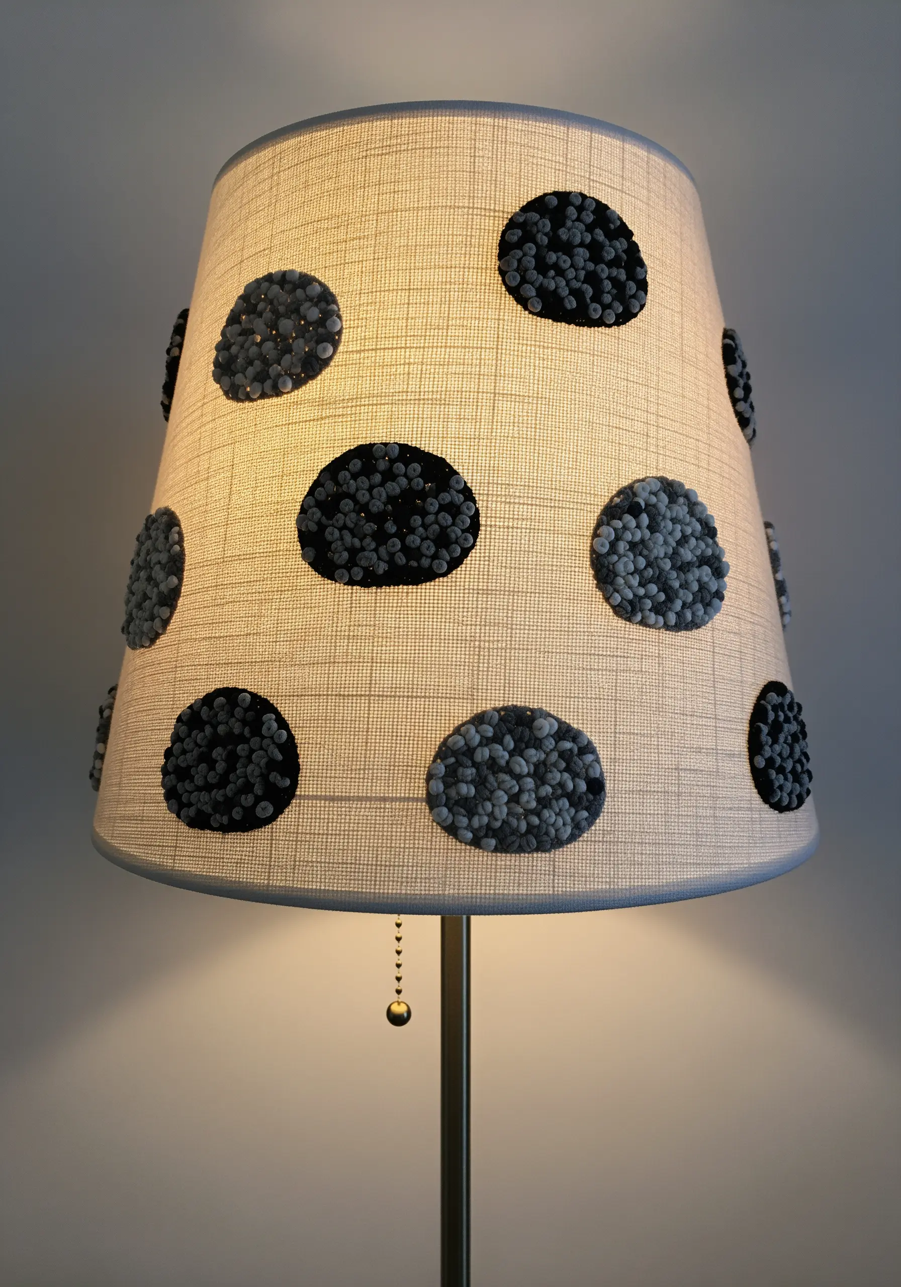 A fabric lampshade decorated with polka dots made from clusters of gray French knots.