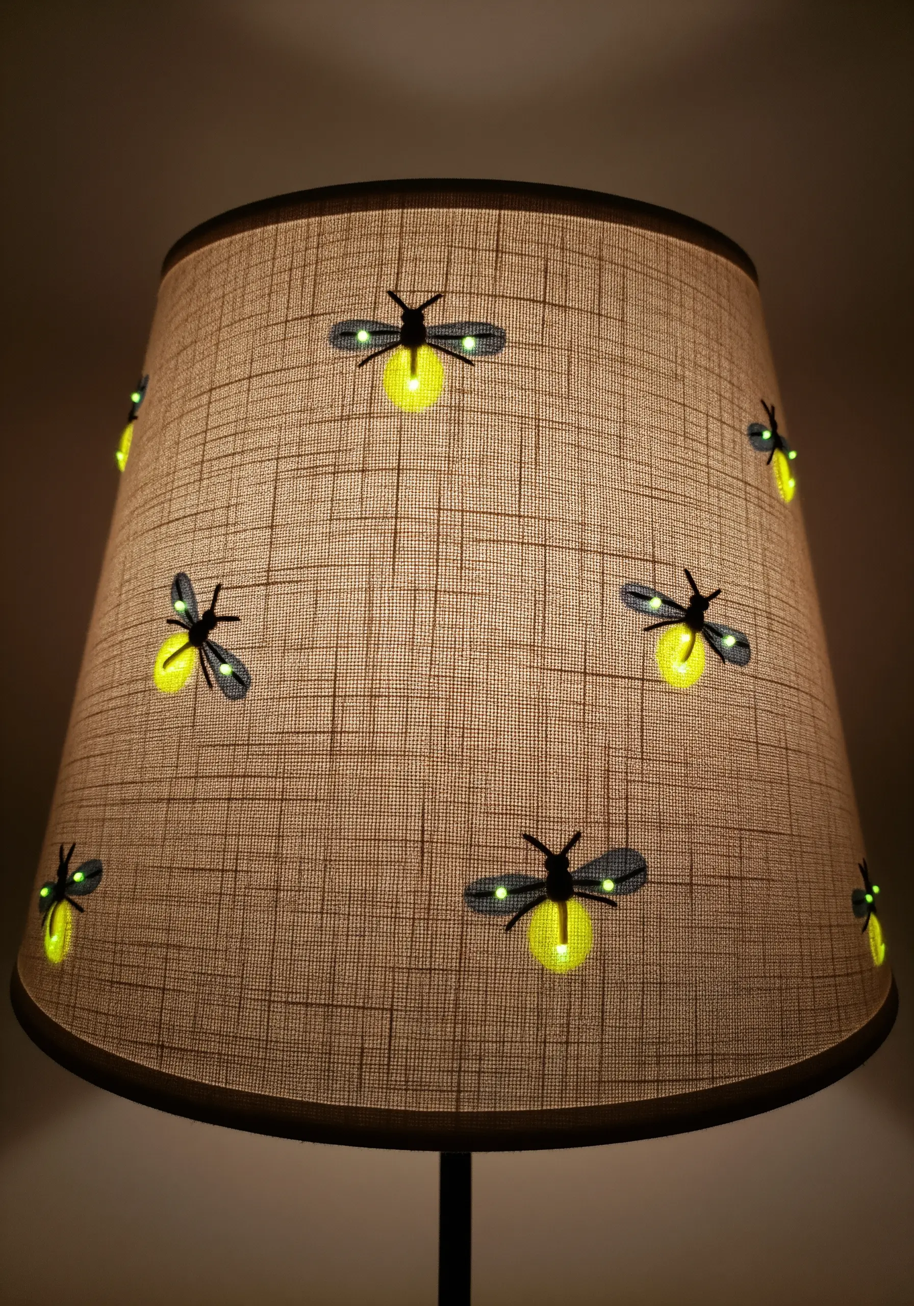 A linen lampshade embroidered with fireflies whose bodies glow a soft yellow-green in the dark.