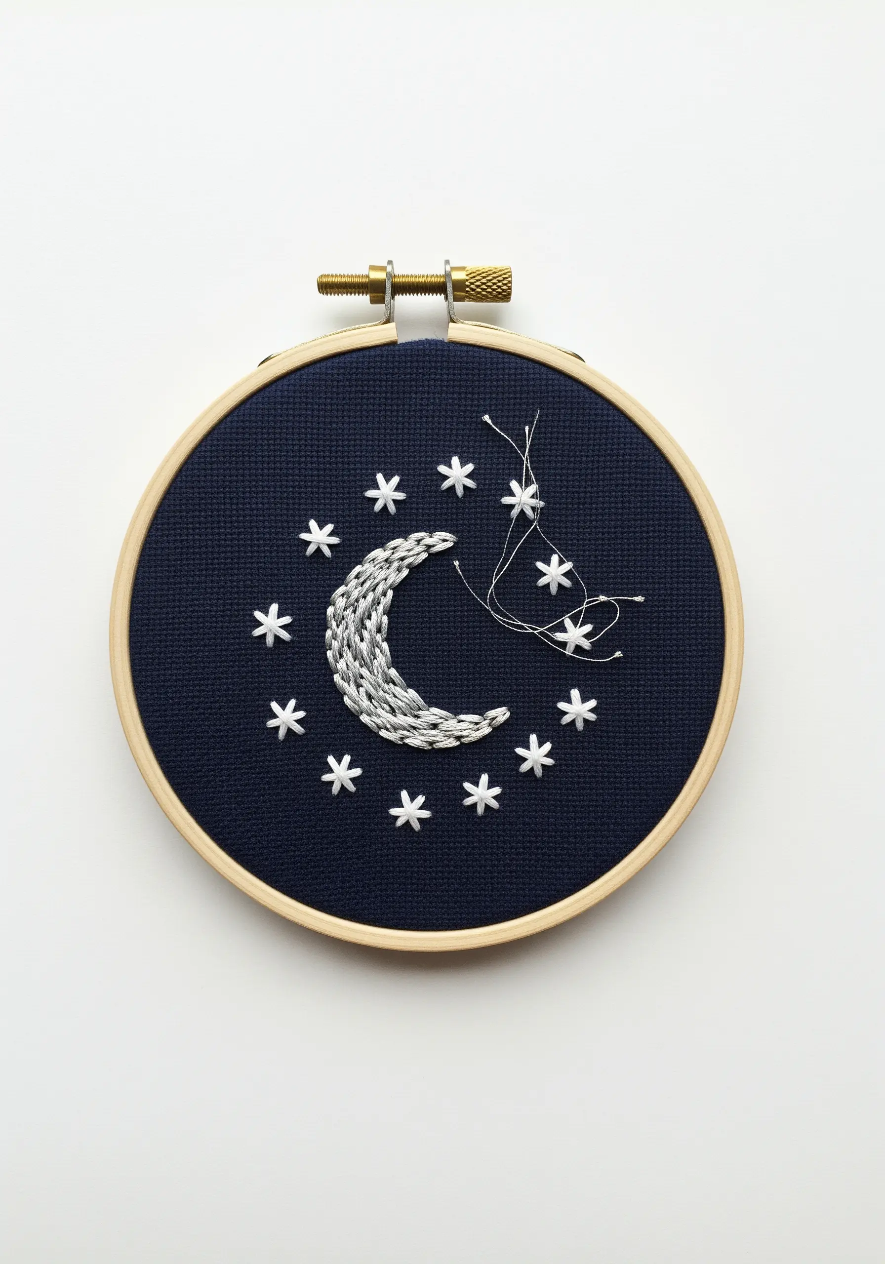 A textured silver crescent moon and stars embroidered with metallic thread on dark navy fabric.