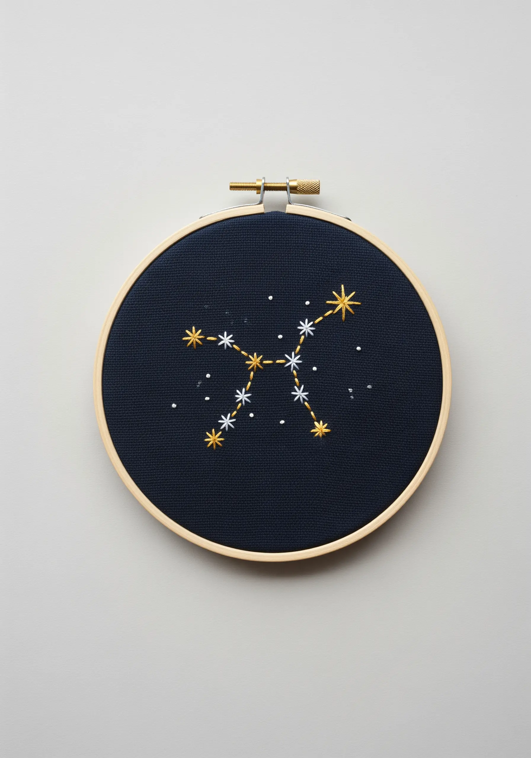 Gold and white embroidered constellation on dark navy blue fabric in a hoop.