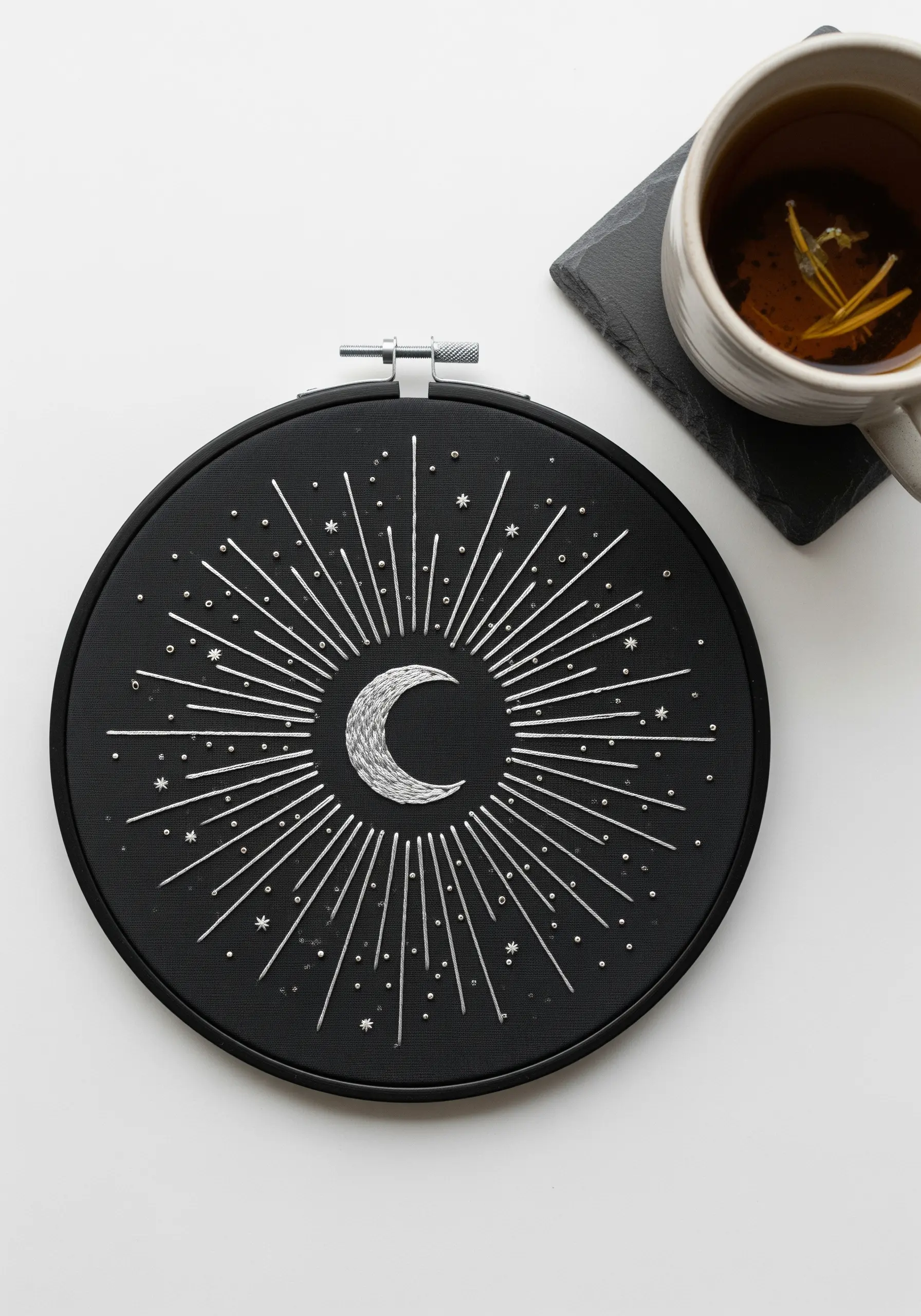 A celestial moon and starburst embroidered in white thread on a black hoop.