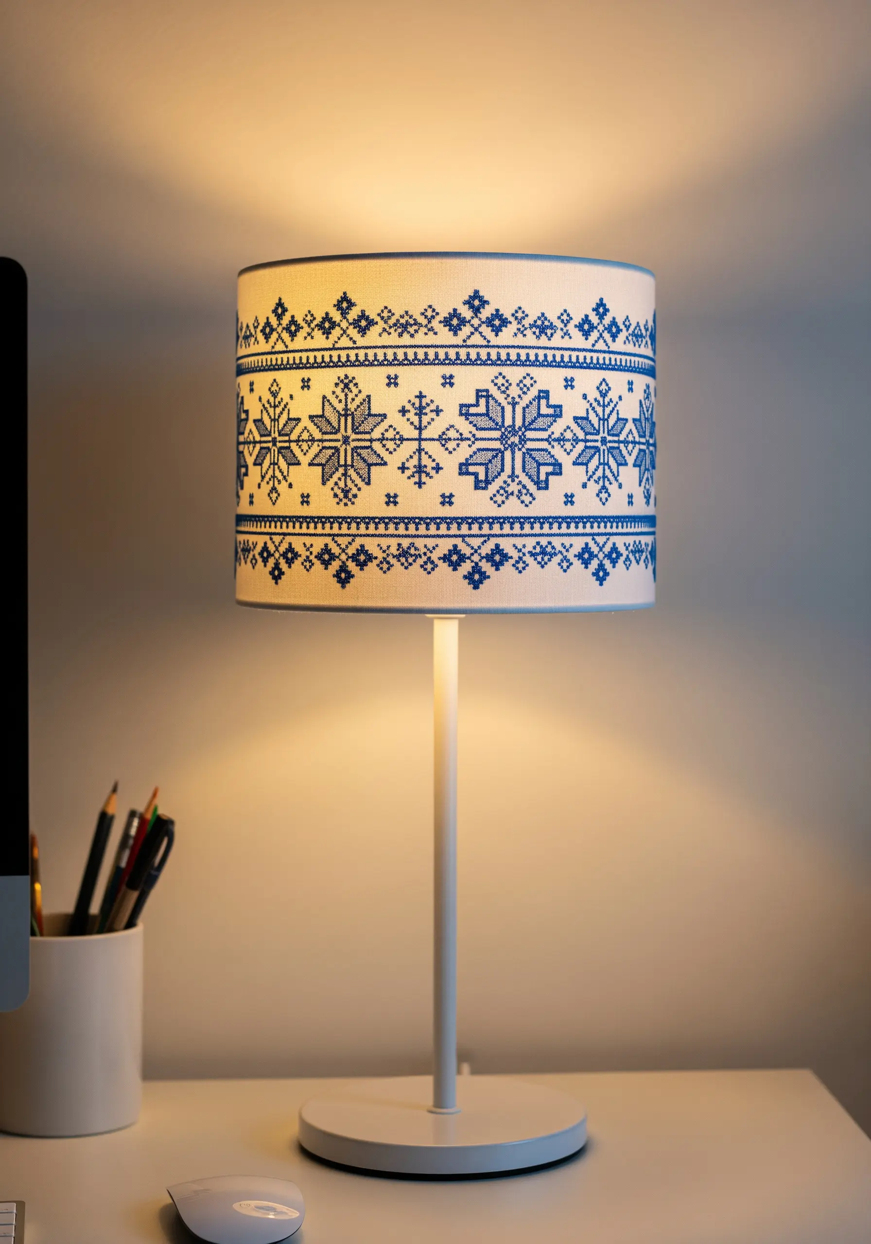A white desk lamp with a lampshade decorated with a blue geometric cross-stitch snowflake pattern.