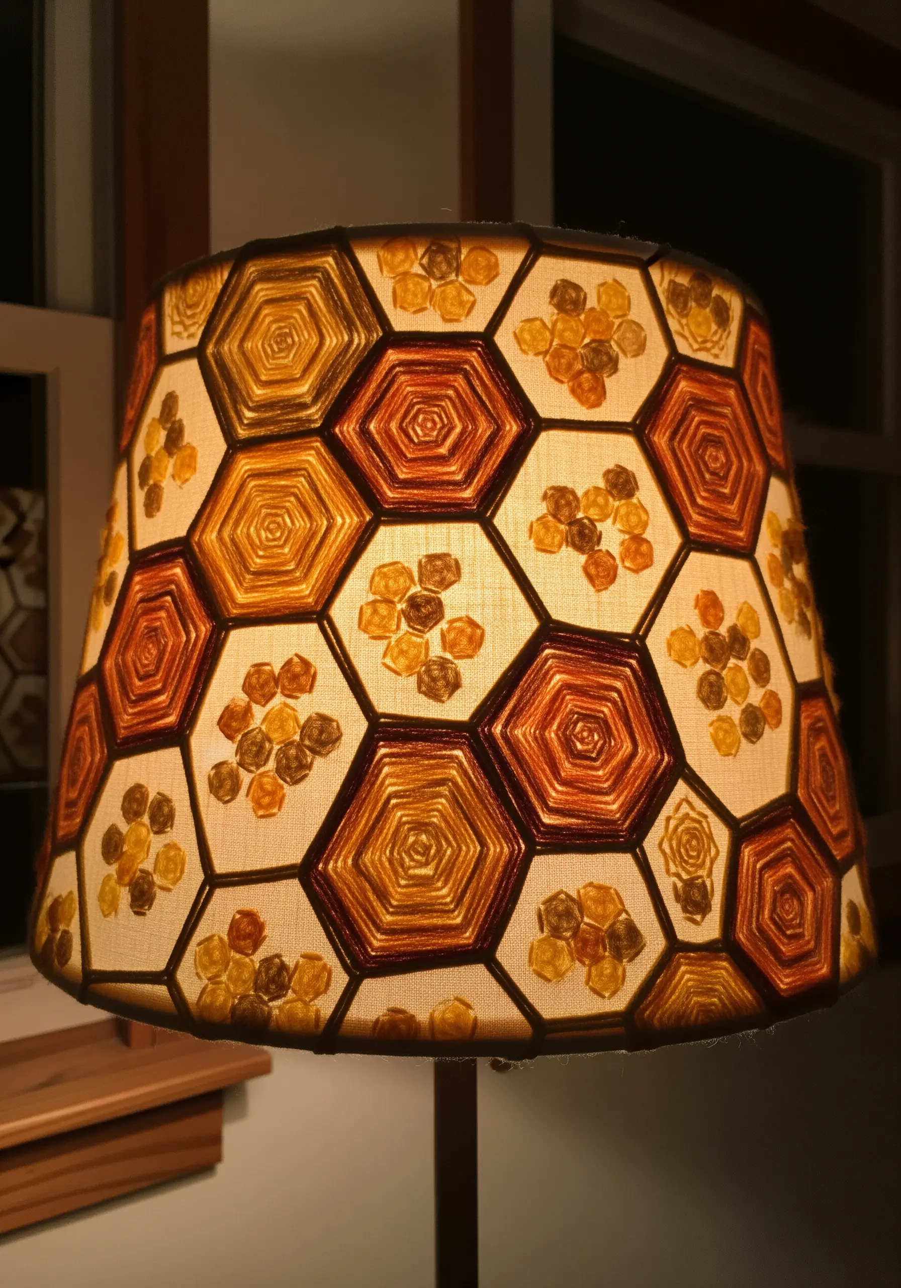 A lampshade decorated with an embroidered honeycomb pattern in warm orange and yellow tones.