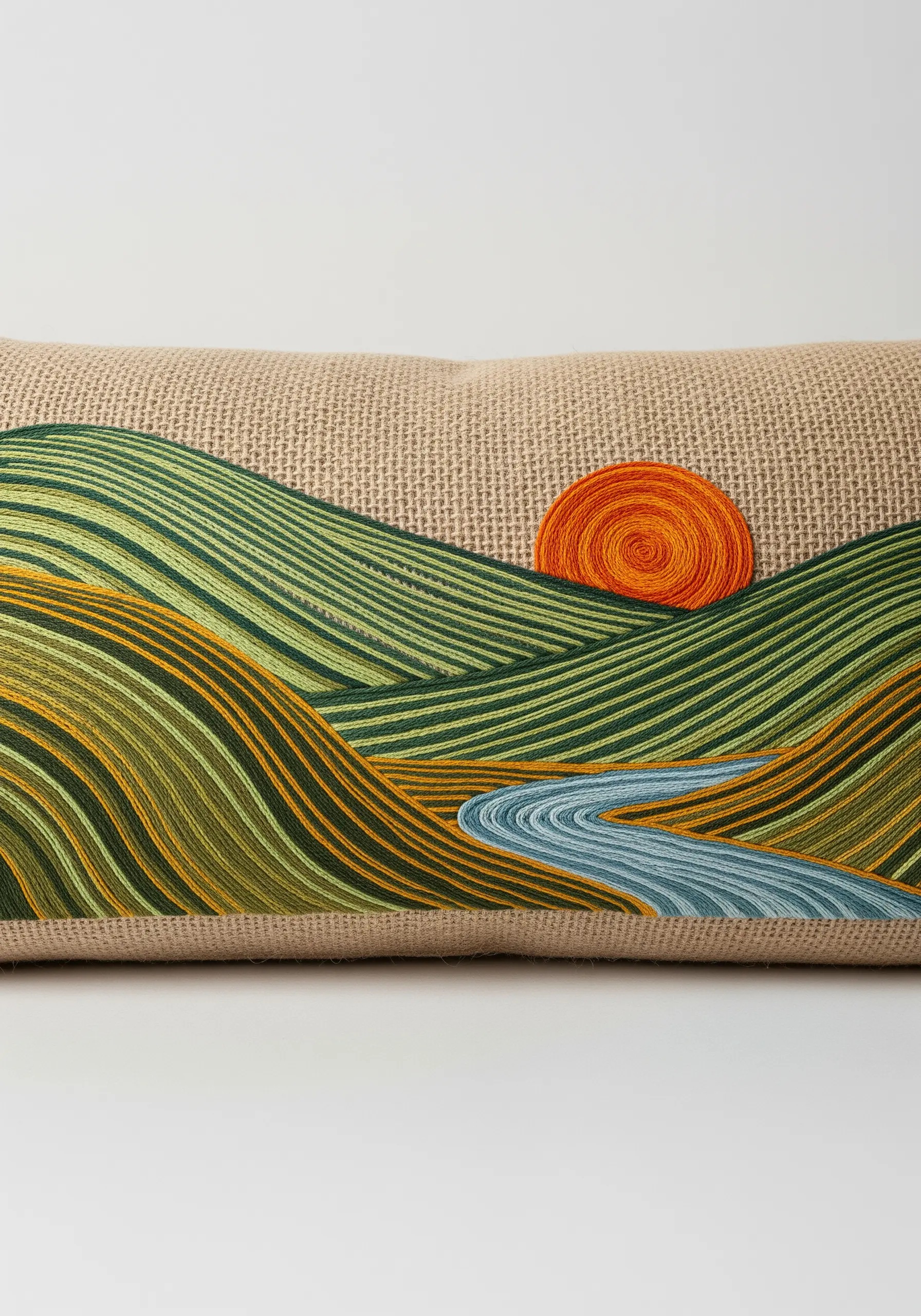 An embroidered landscape of rolling hills and a couched spiral sun on a burlap pillow.