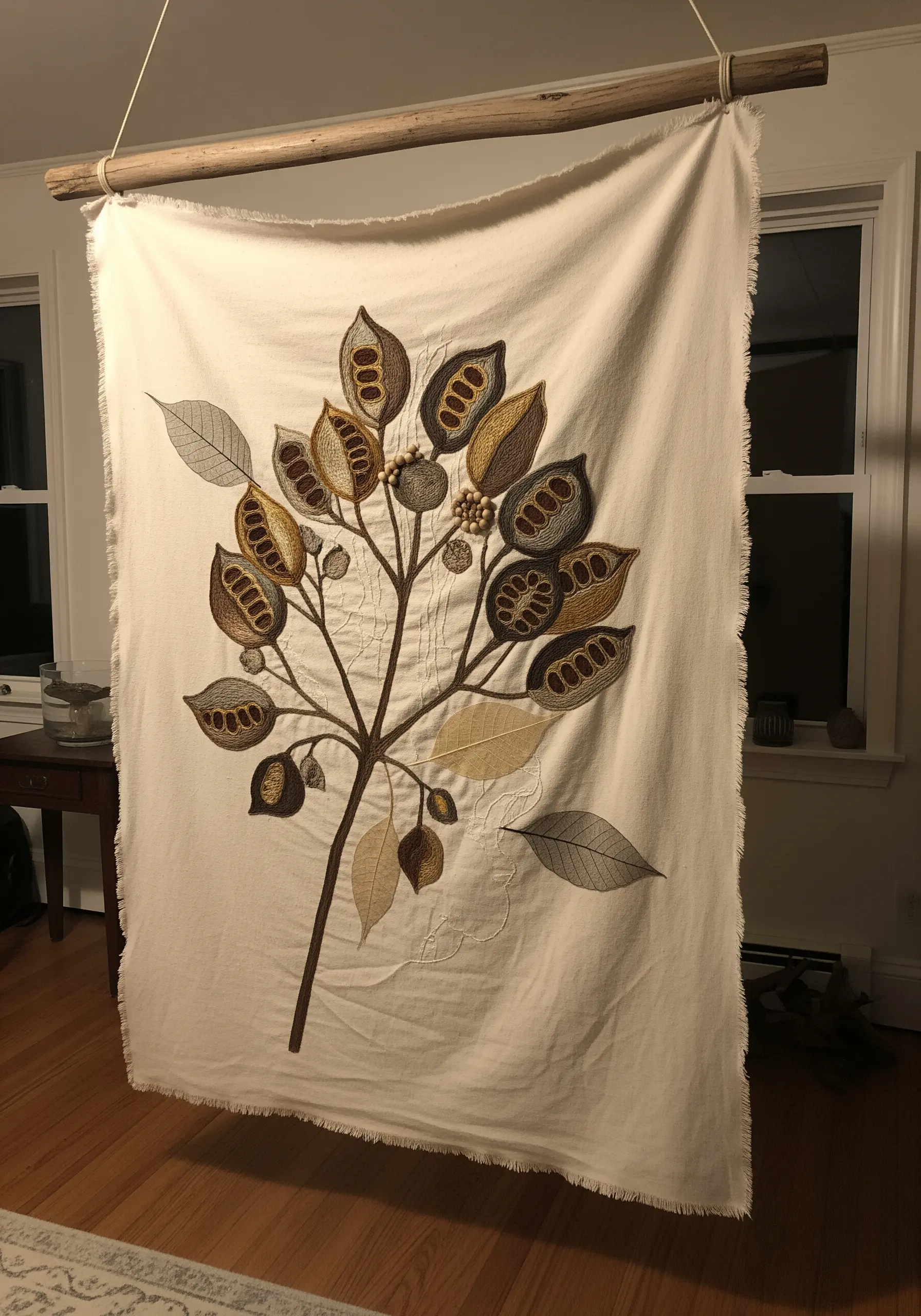 A large botanical wall hanging on raw-edge fabric, featuring embroidered seed pods.