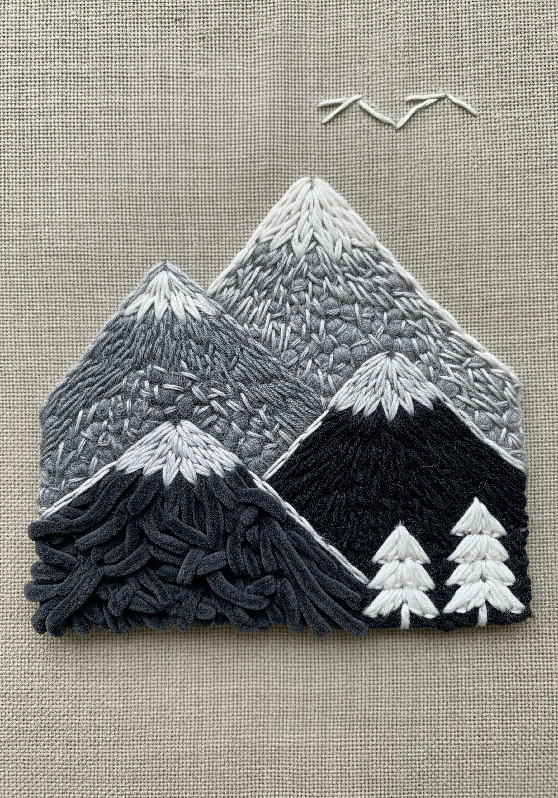 A monochrome mountain range embroidered with various textural stitches to create depth.