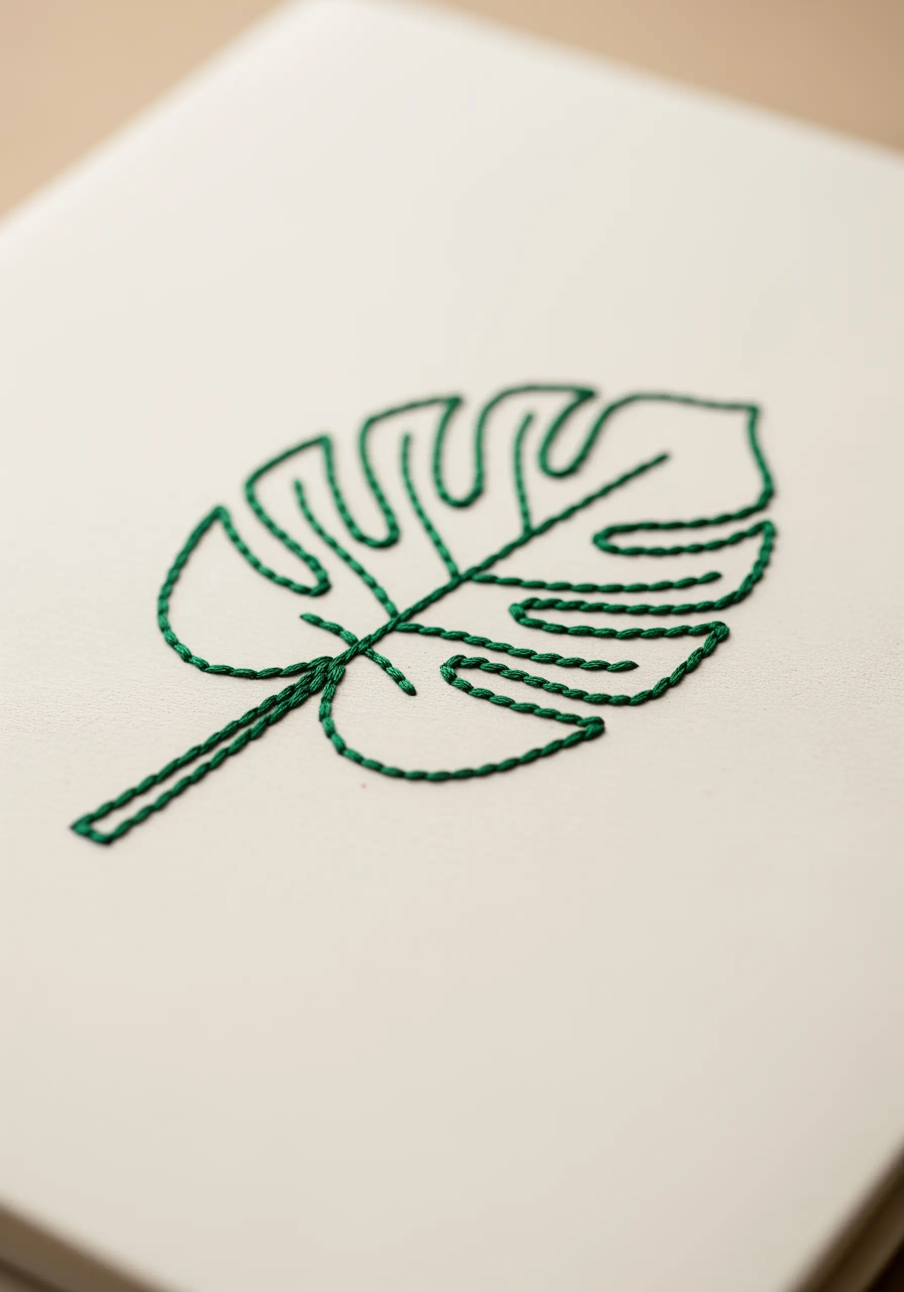 The outline of a monstera leaf embroidered with a green chain stitch on a white journal.