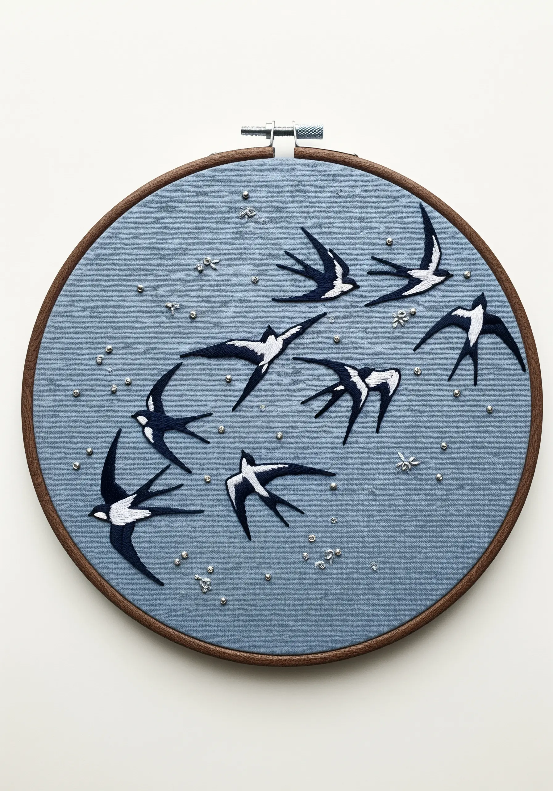Embroidered black and white swallows flying across a dusty blue fabric hoop.