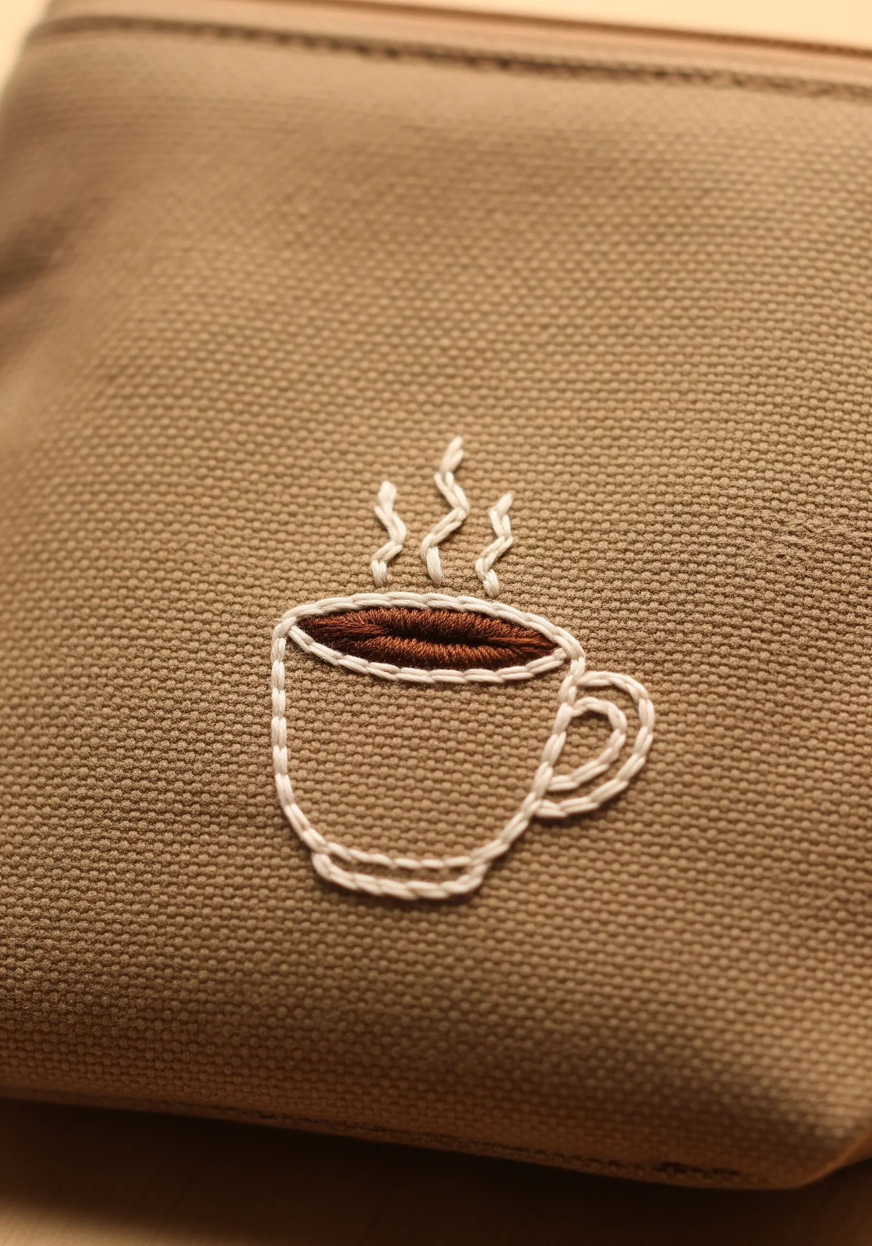 An embroidered coffee cup with brown satin stitch coffee and white outline and steam.