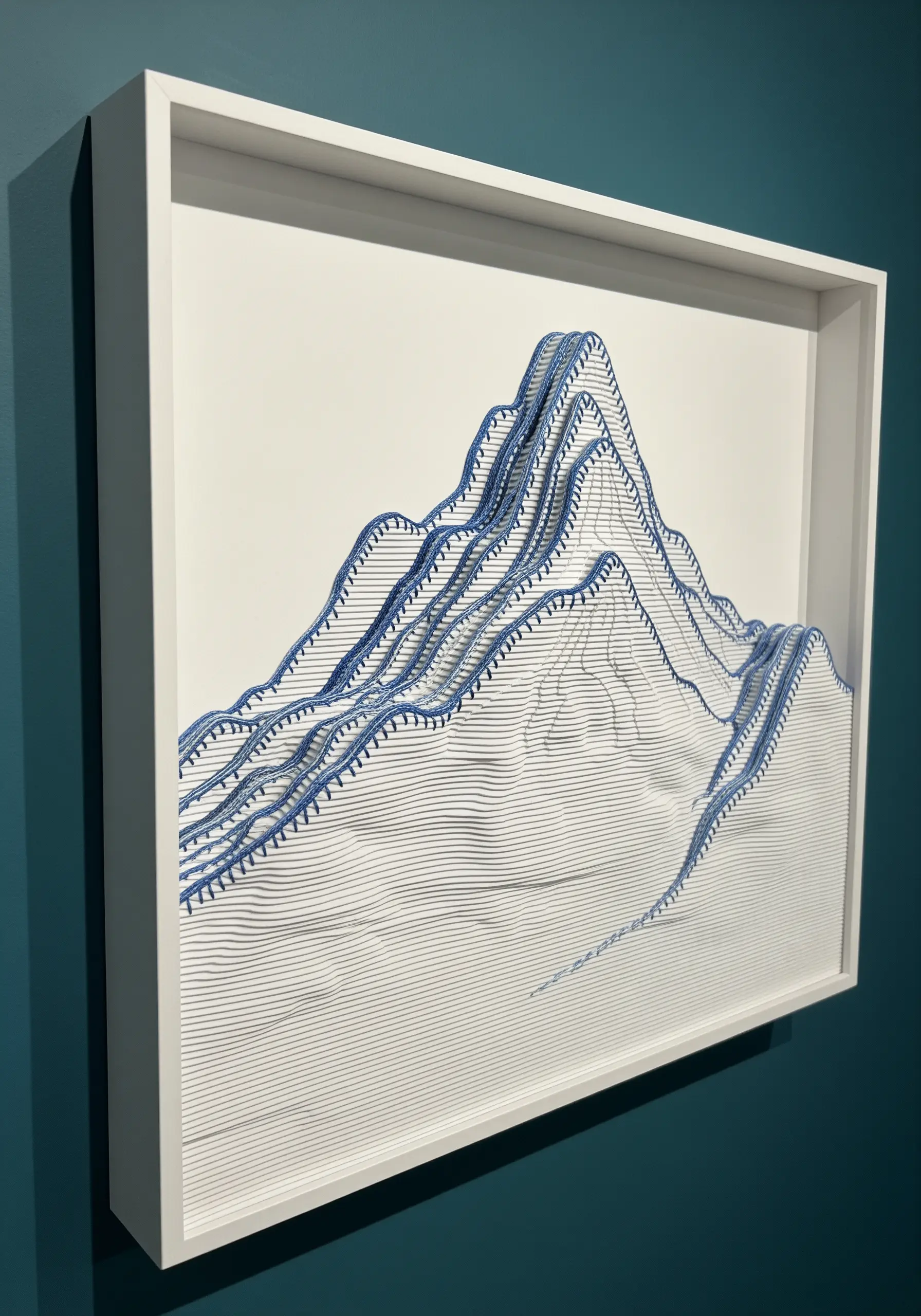 A 3D topographic mountain scene made from layers of cut paper and thread, framed in a white box.