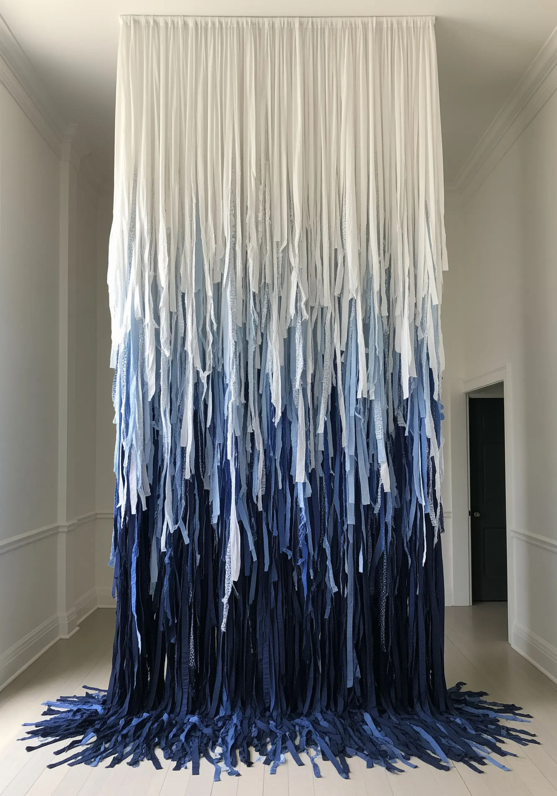 A floor-to-ceiling installation of hanging fabric strips, transitioning in a gradient from white to dark blue.