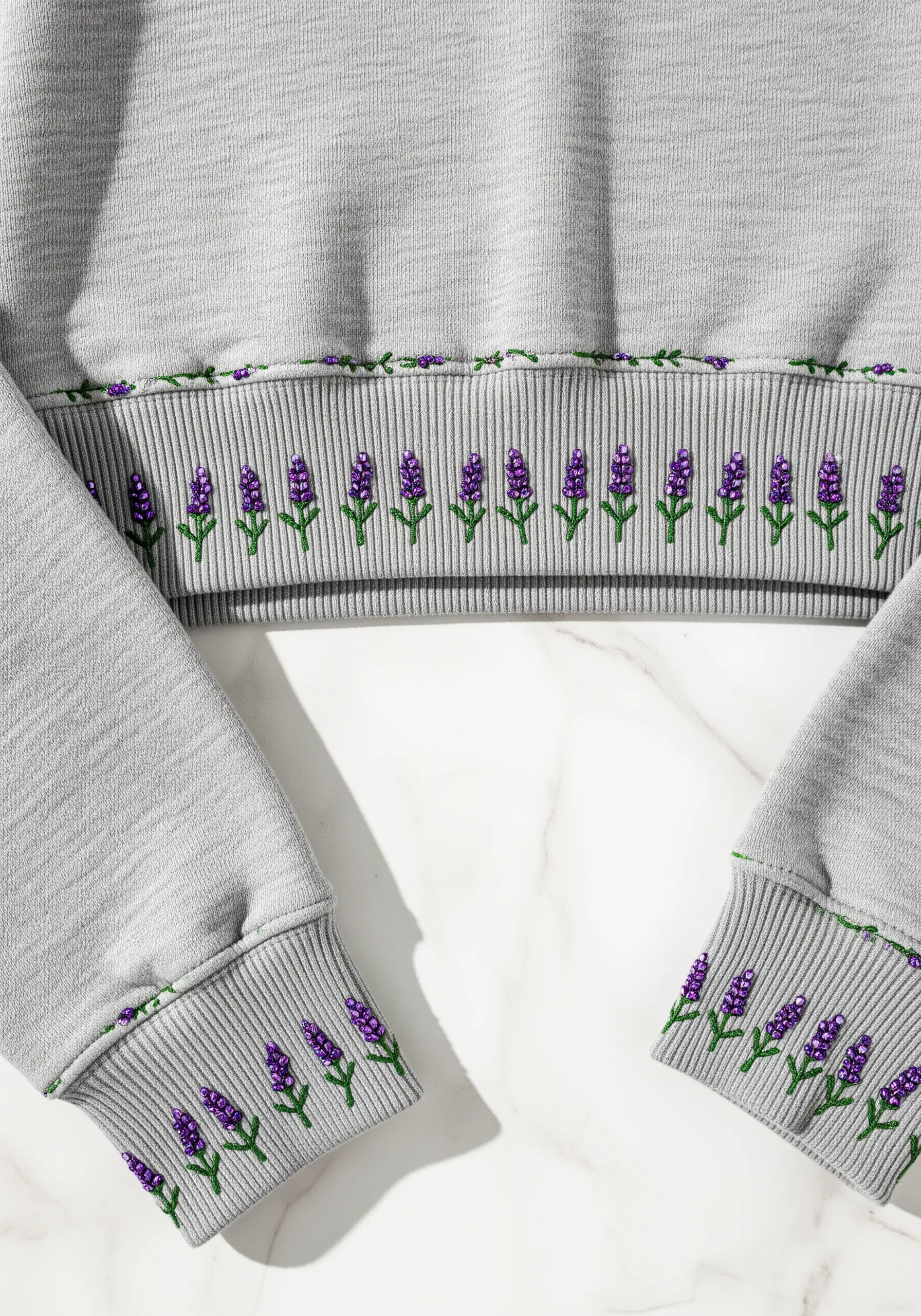 Lavender sprig embroidery with purple beads on the cuffs and hem of a grey sweatshirt
