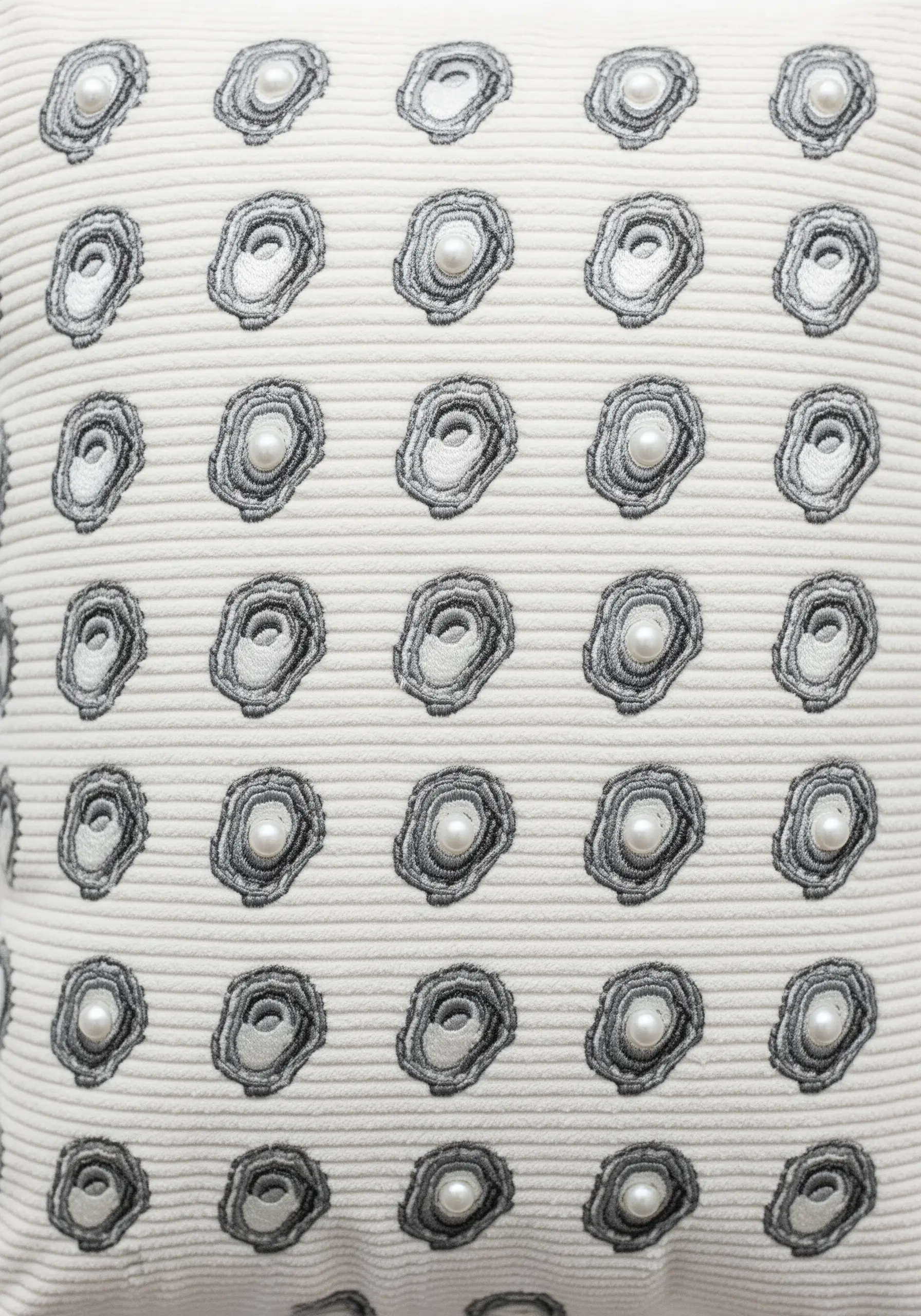A grid pattern of embroidered oyster shells, each with a pearl bead center, on a corduroy pillow