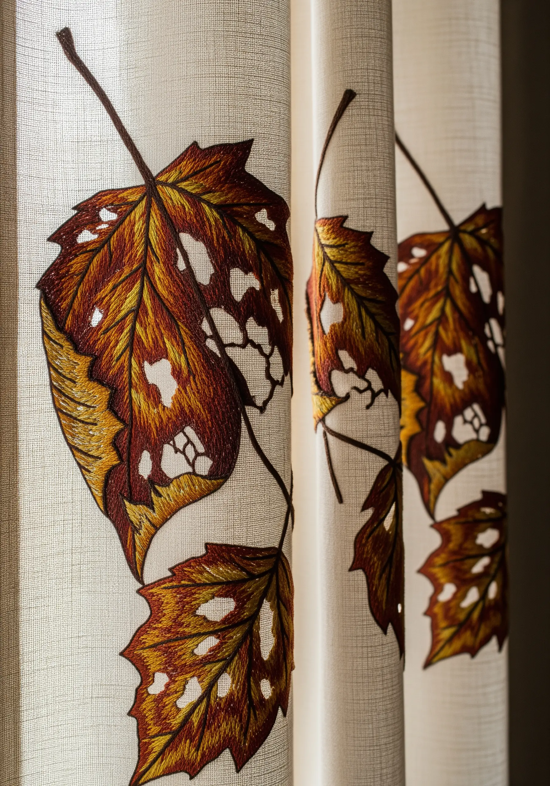 Embroidered autumn leaves on a curtain, with cutwork creating open spaces in the design.