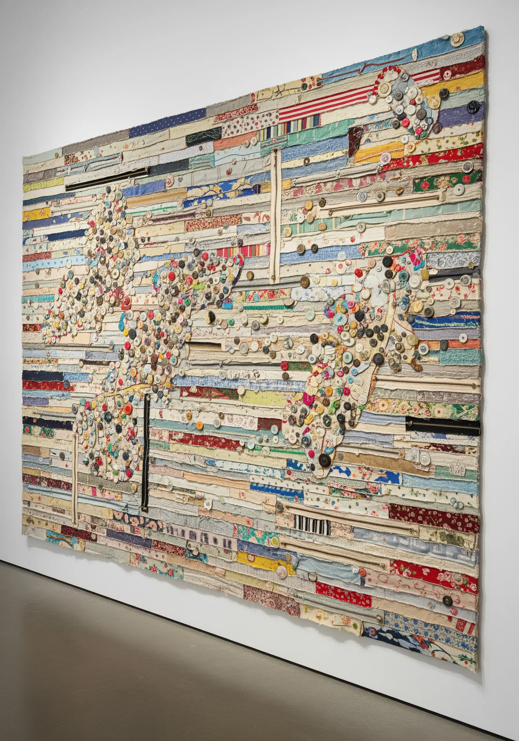 A large wall tapestry made from horizontal strips of fabric, embellished with clusters of buttons.