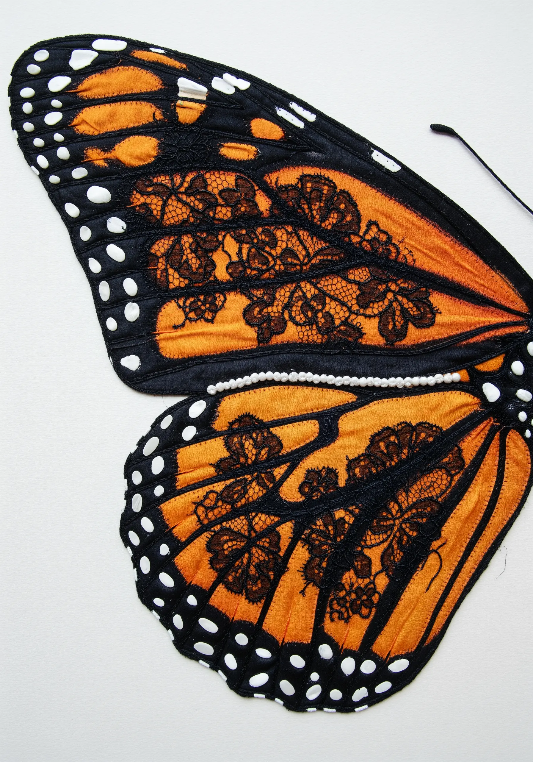 A Monarch butterfly wing made from orange satin and a black floral lace overlay.