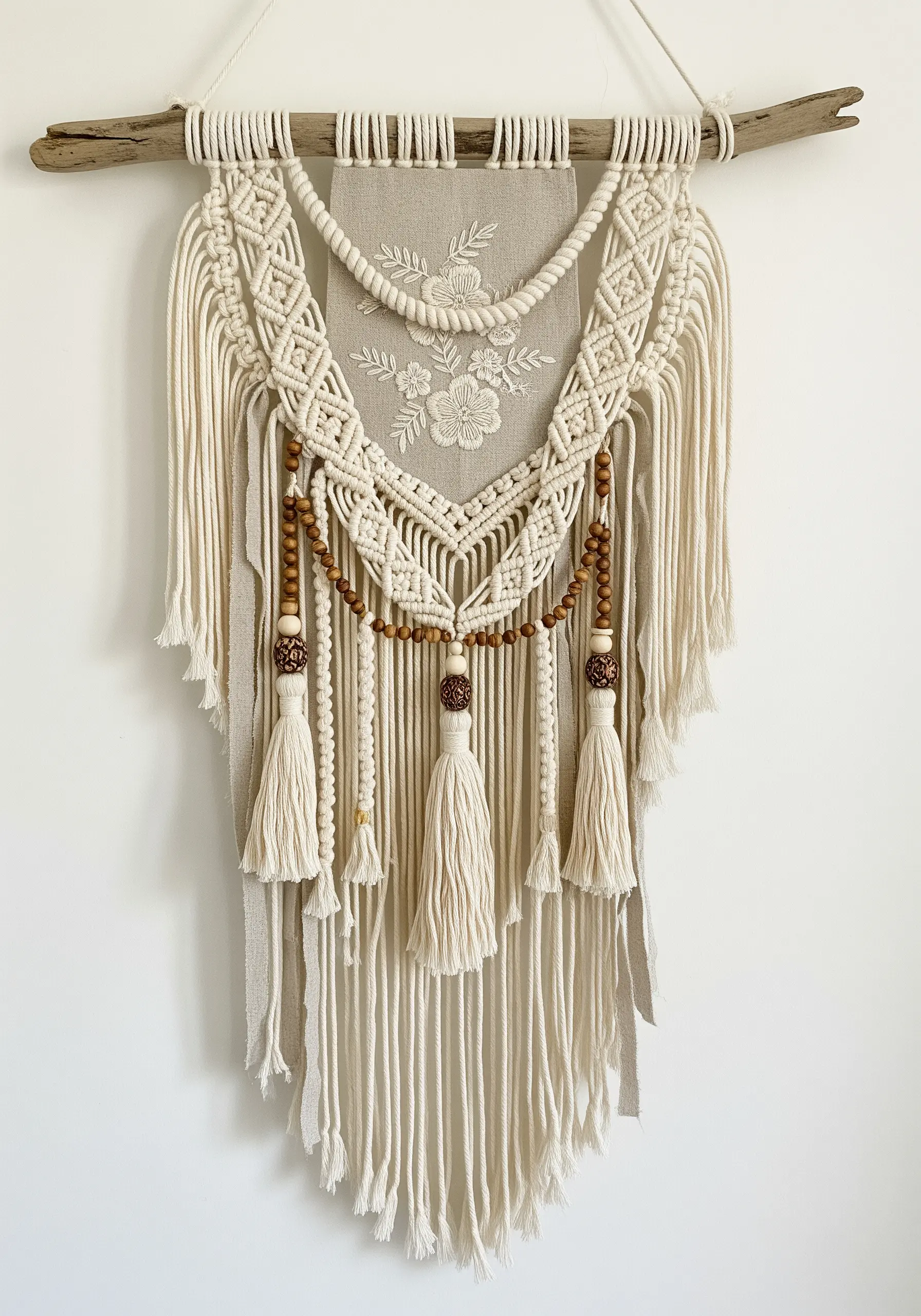 A wall hanging combining a central embroidered floral panel with surrounding macrame knots.