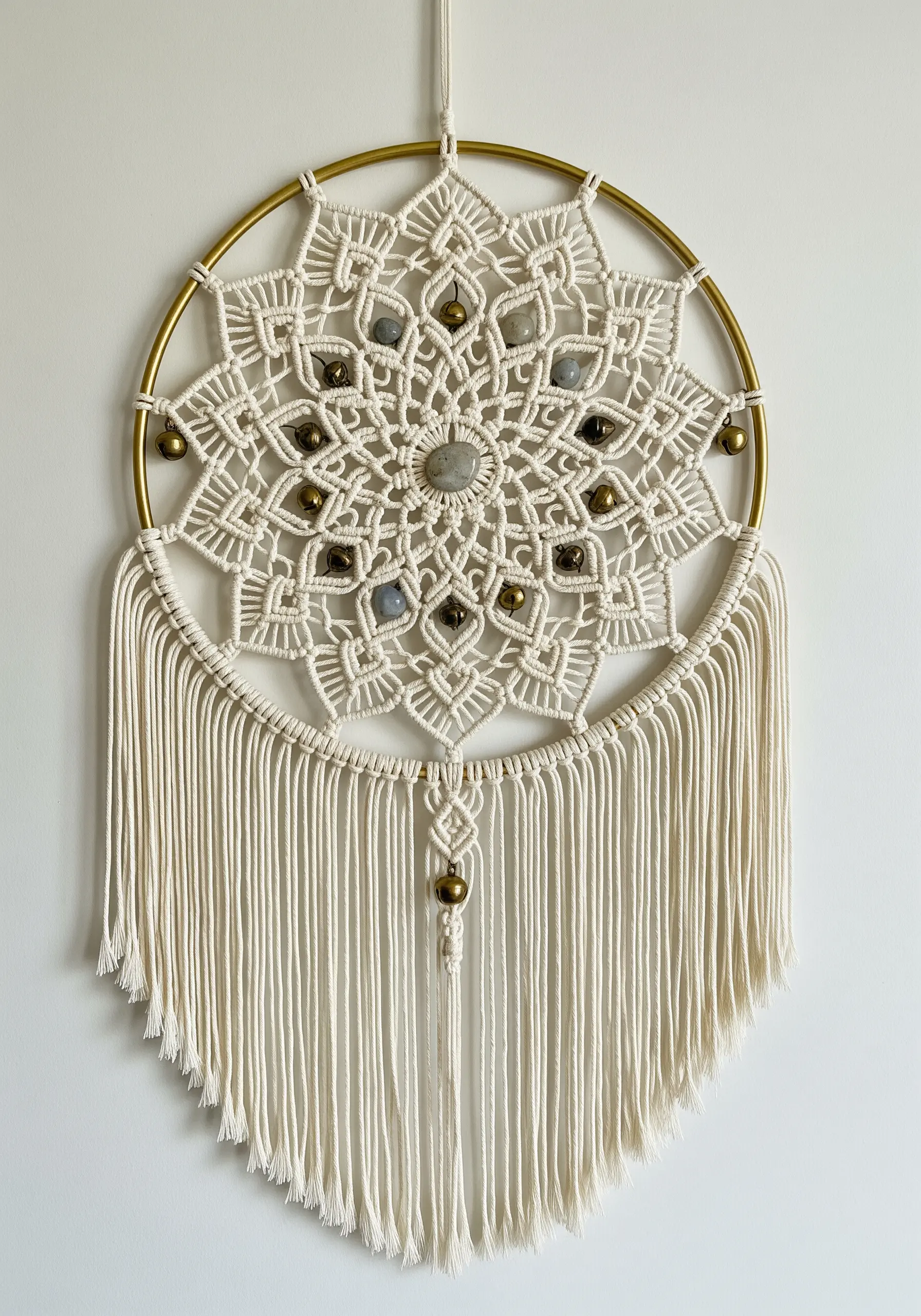 Macrame mandala in a gold hoop with stone beads and small brass bells.