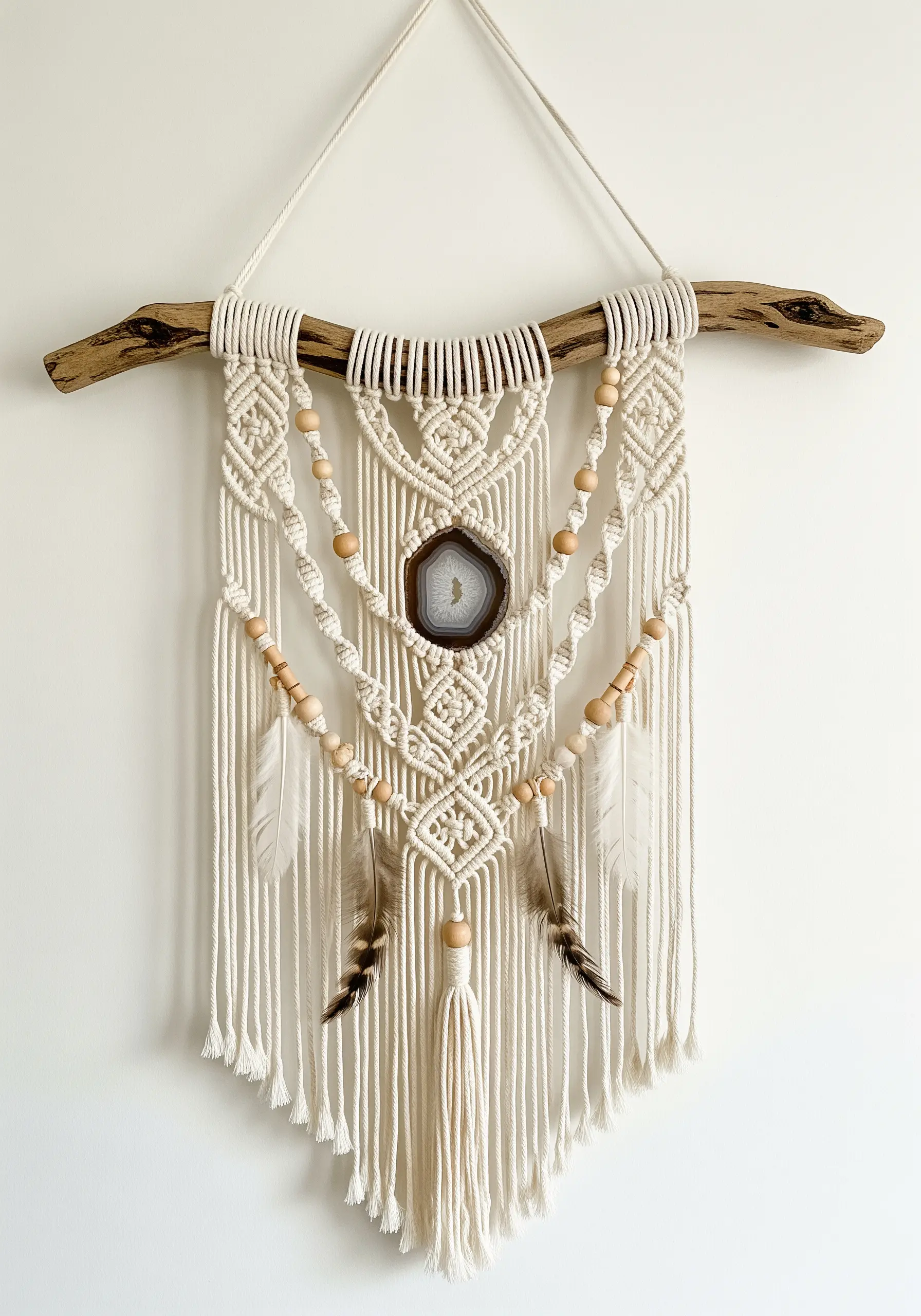 Macrame wall hanging on driftwood, featuring a central agate slice, wooden beads, and feathers.