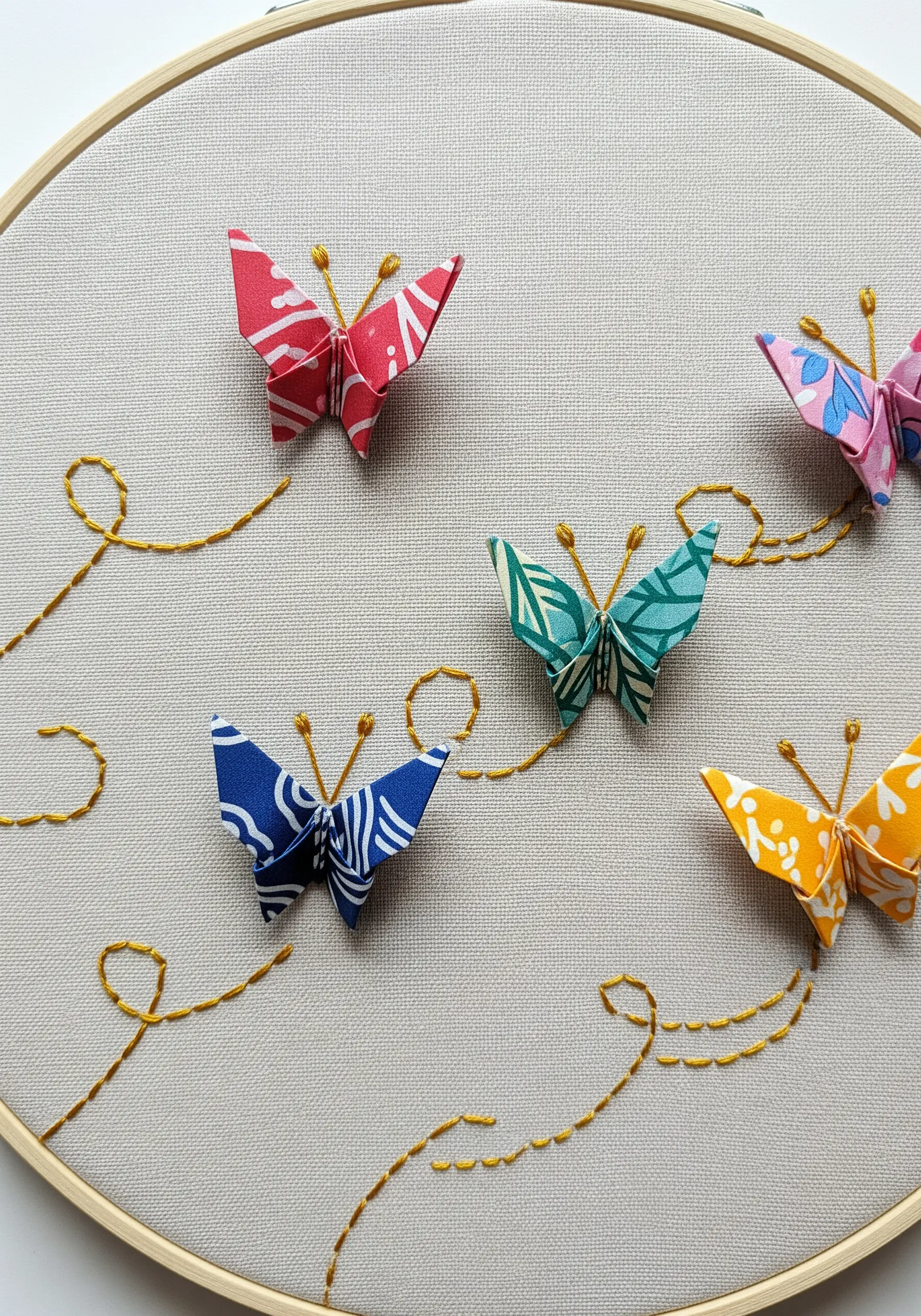 Four colorful origami butterflies appliquéd on linen with stitched flight paths.