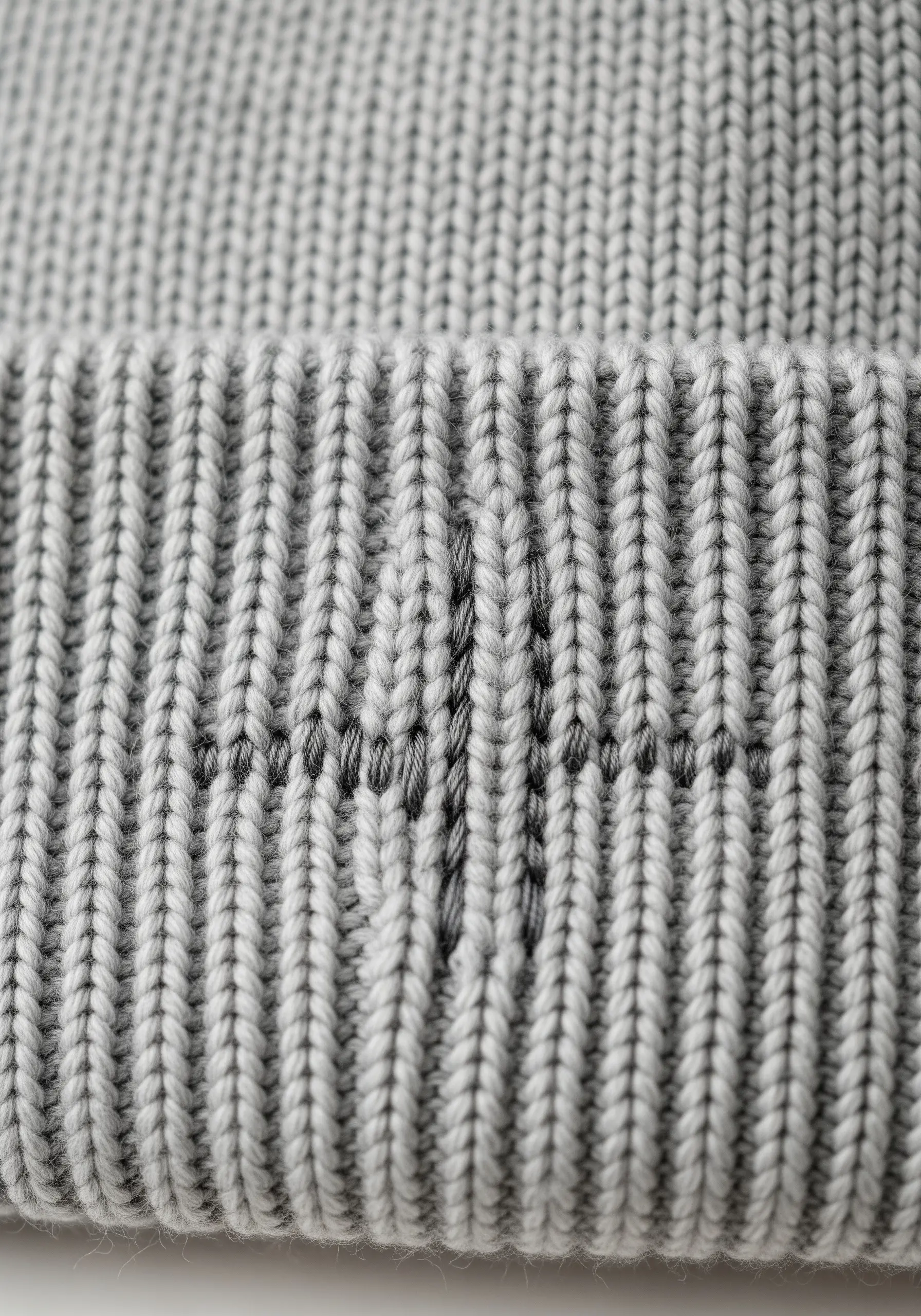 A simple heartbeat line stitched in dark grey thread on the cuff of a ribbed grey beanie.