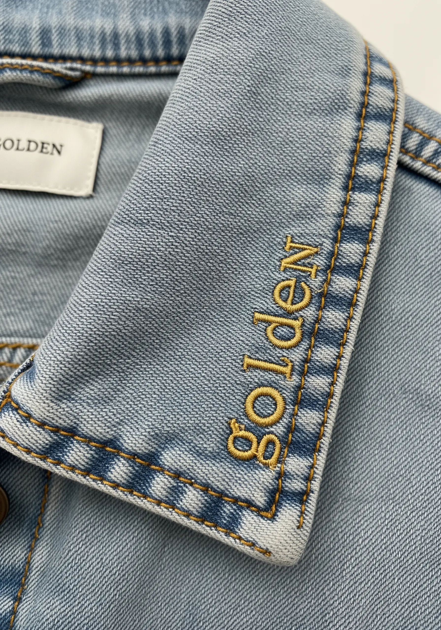 Delicate 'golden' embroidery stitched vertically on a denim collar