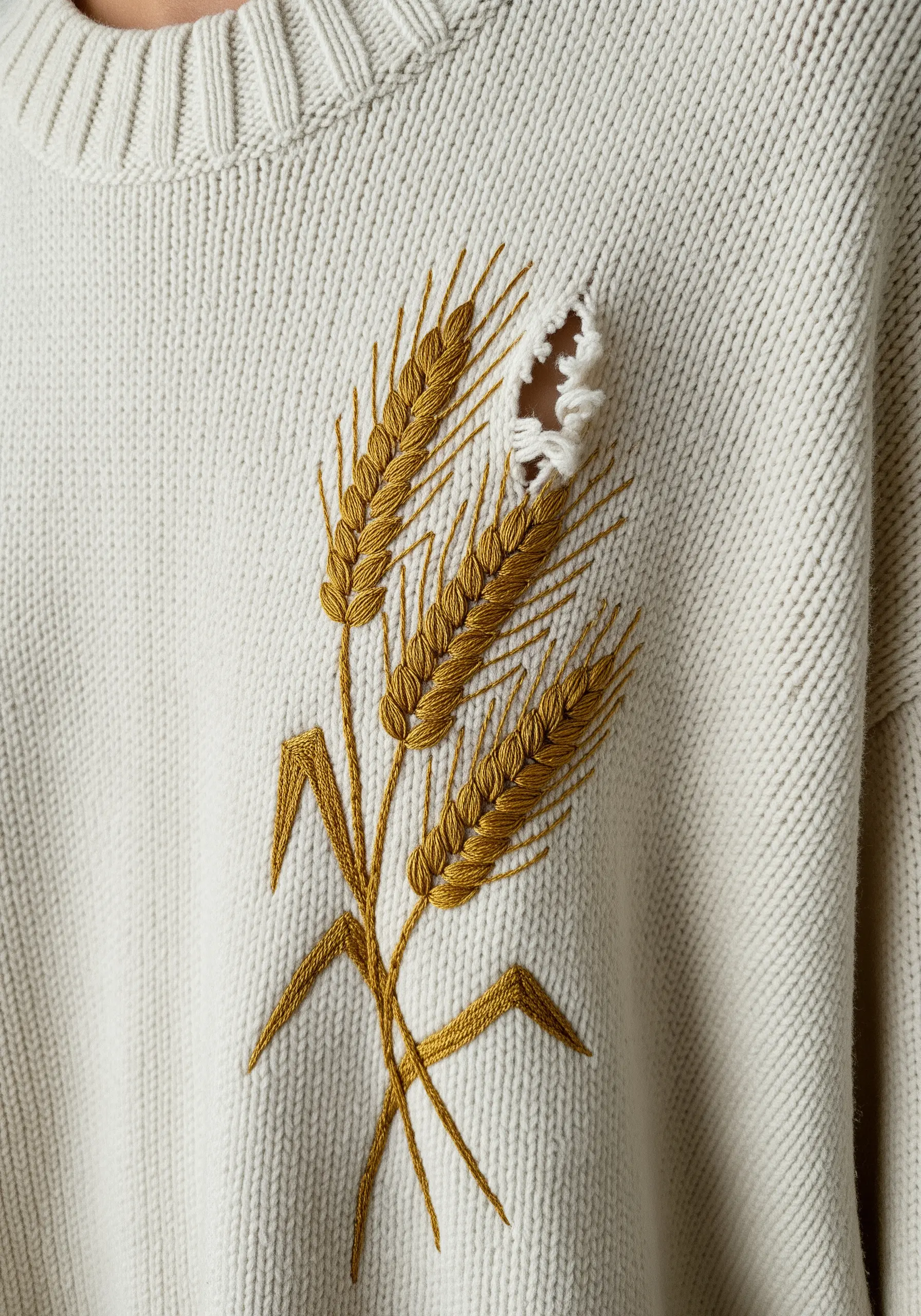 Embroidered golden wheat stalks on a cream sweater, with a small hole cleverly integrated into the design.