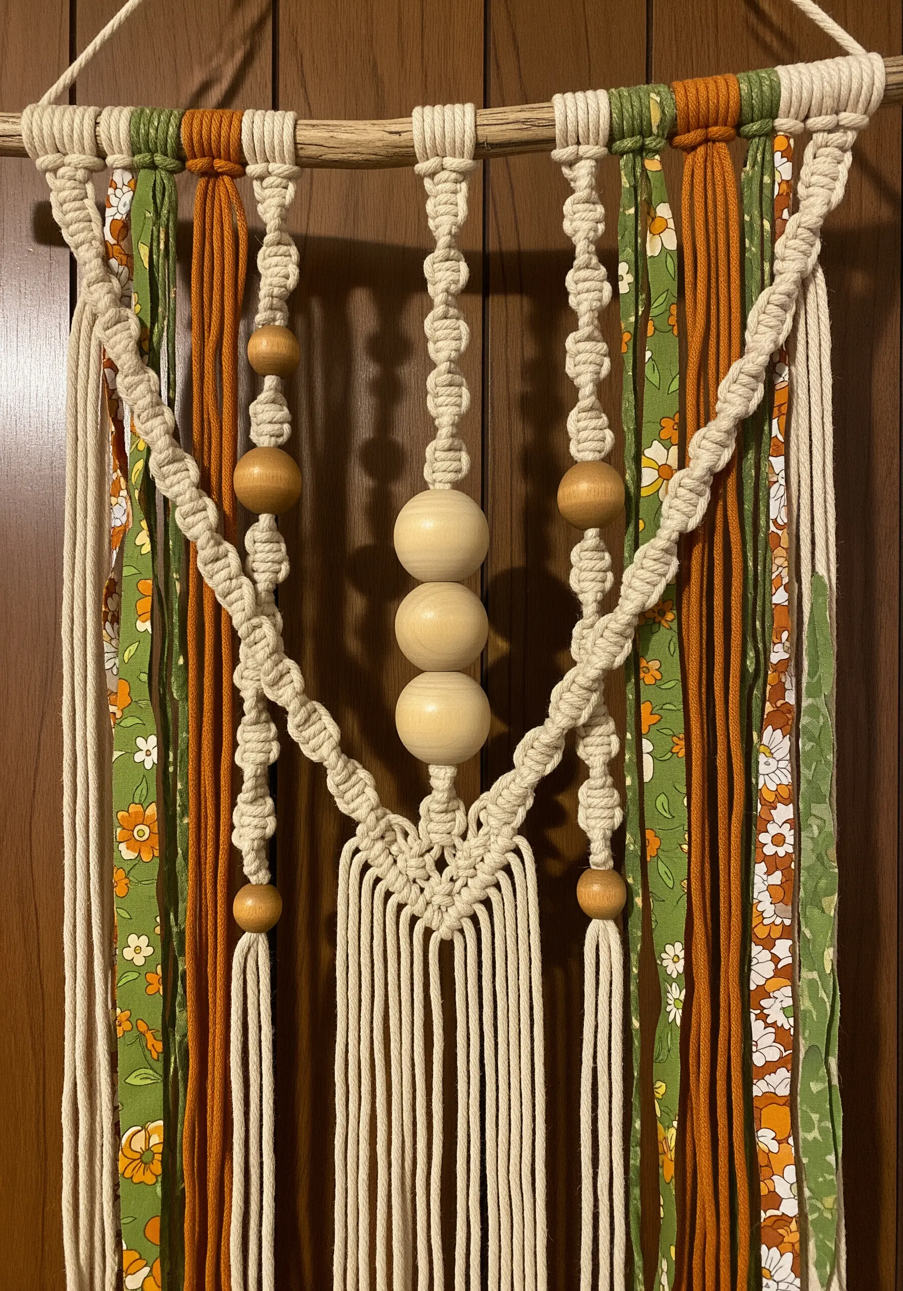 Macrame wall hanging with orange and green floral fabric strips and large wooden beads.