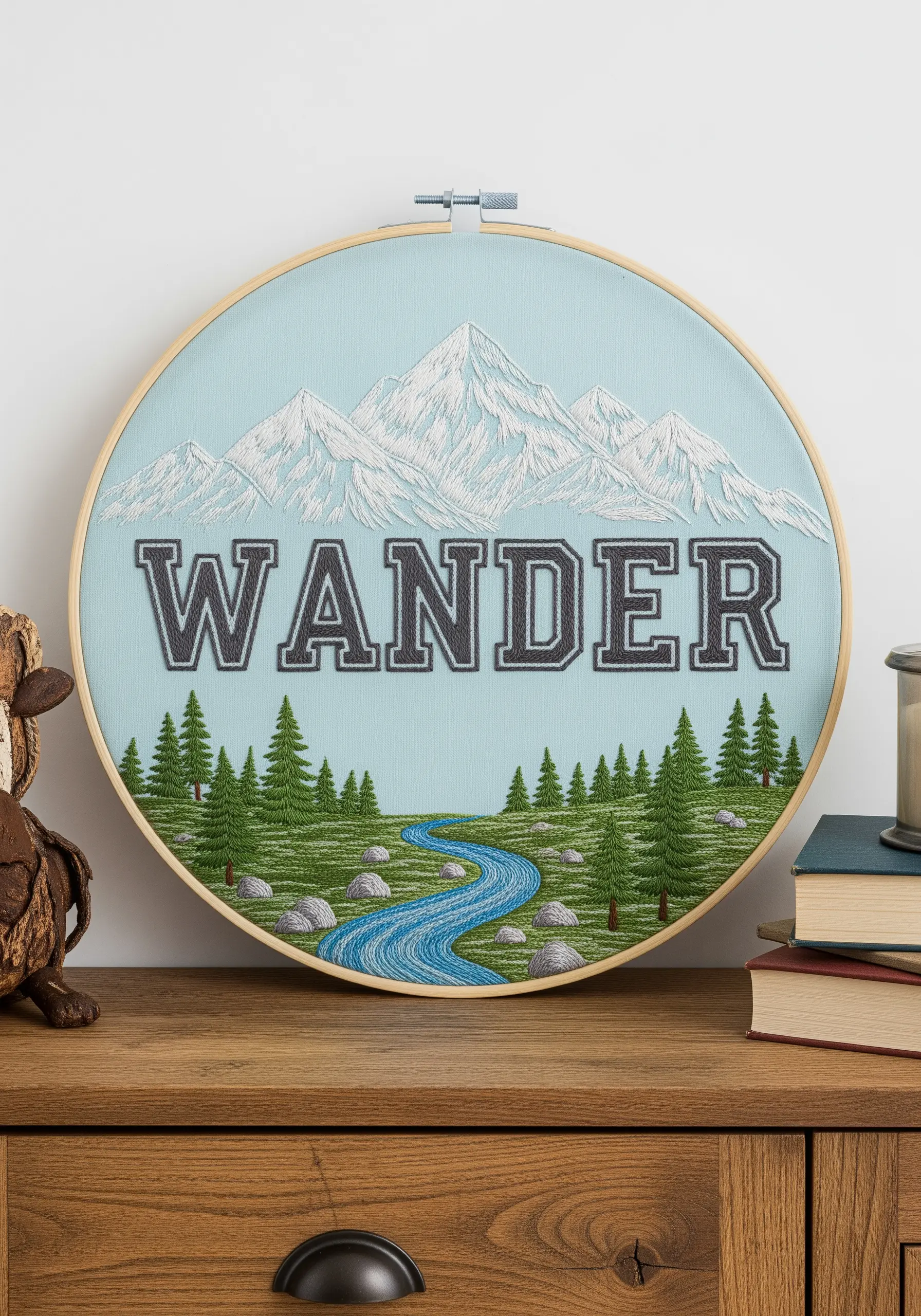 Embroidered landscape with the word 'WANDER' integrated into a mountain and forest scene.