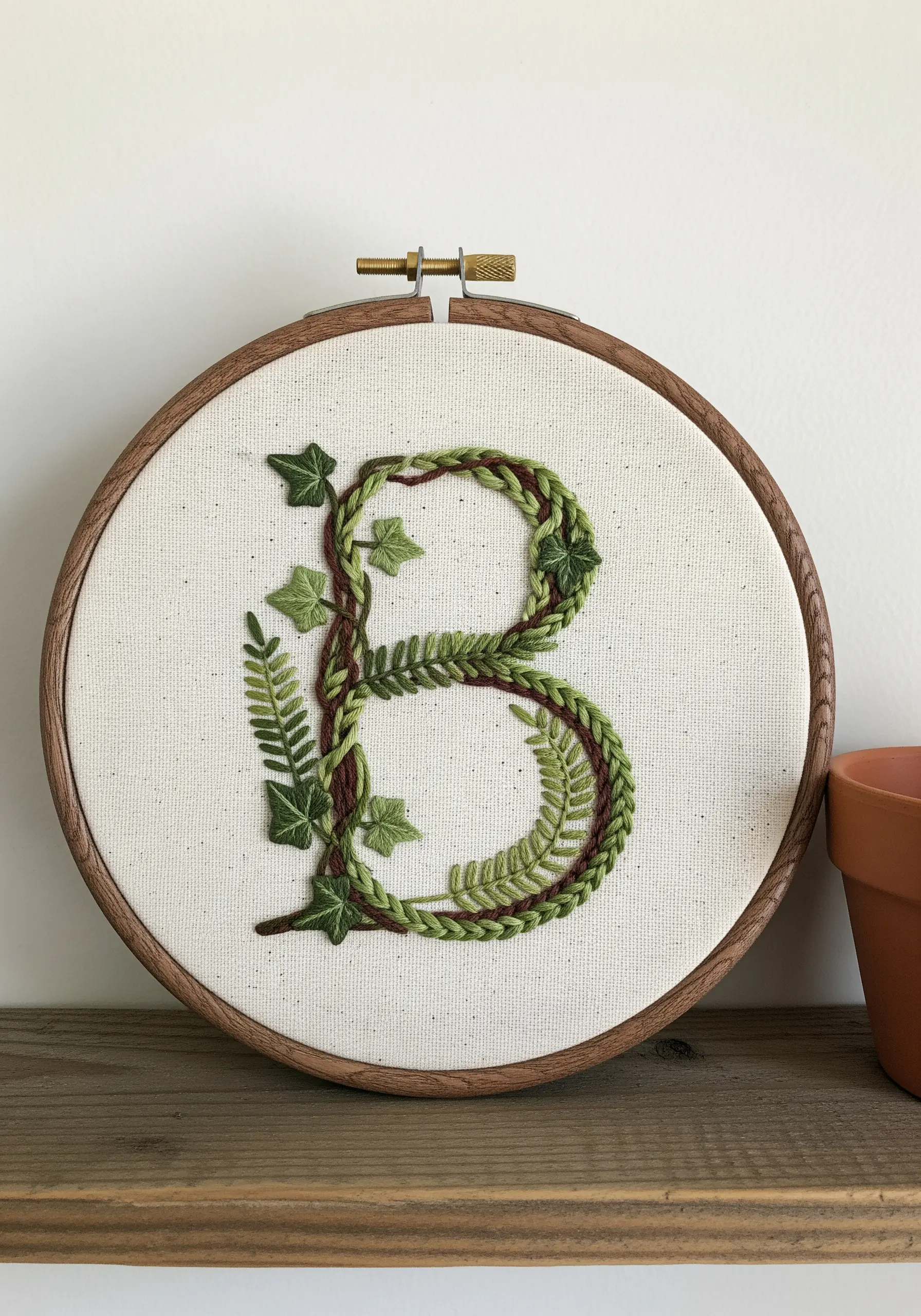 Letter B embroidery with braided green textures, wrapped in dark vines with ferns and ivy.