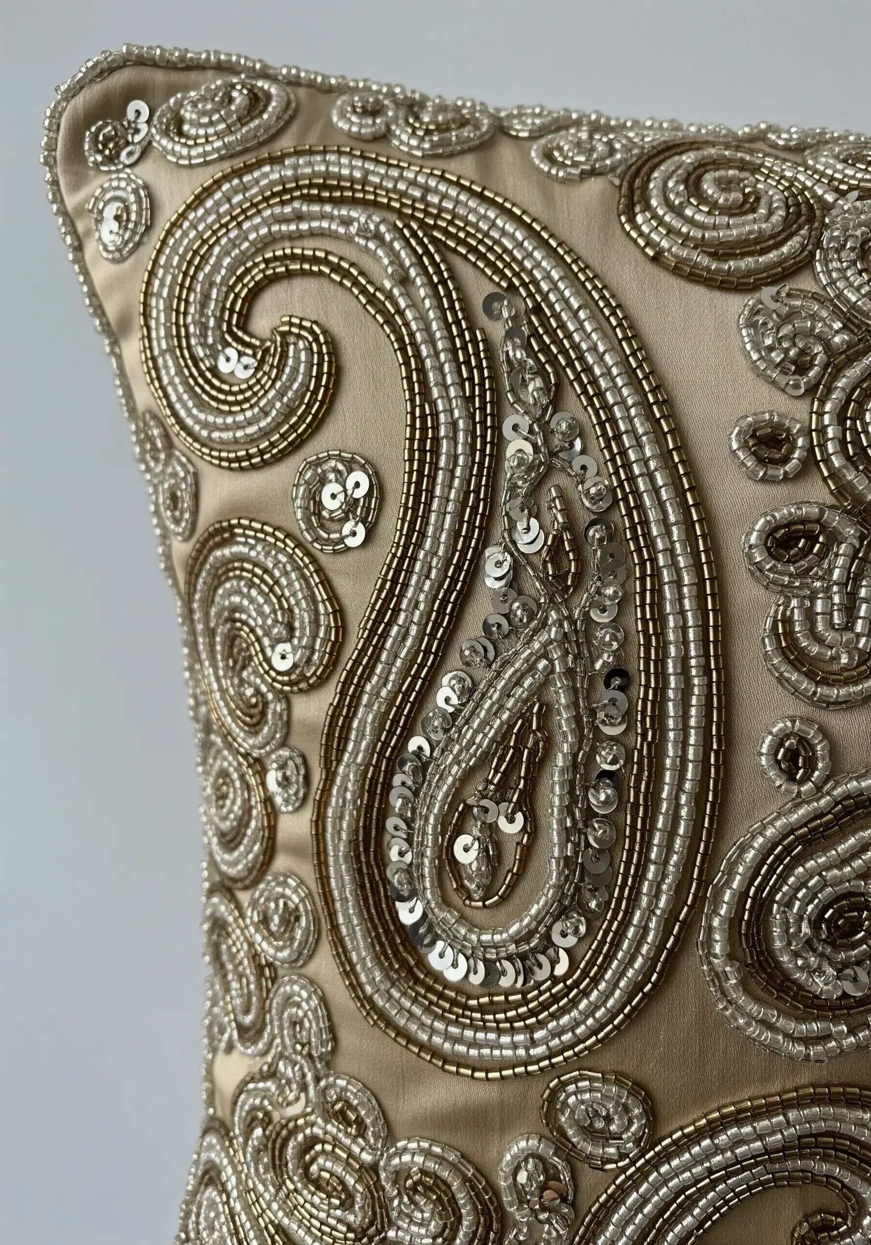 A detailed paisley design on a silk cushion, embellished with silver and gold beads and sequins.
