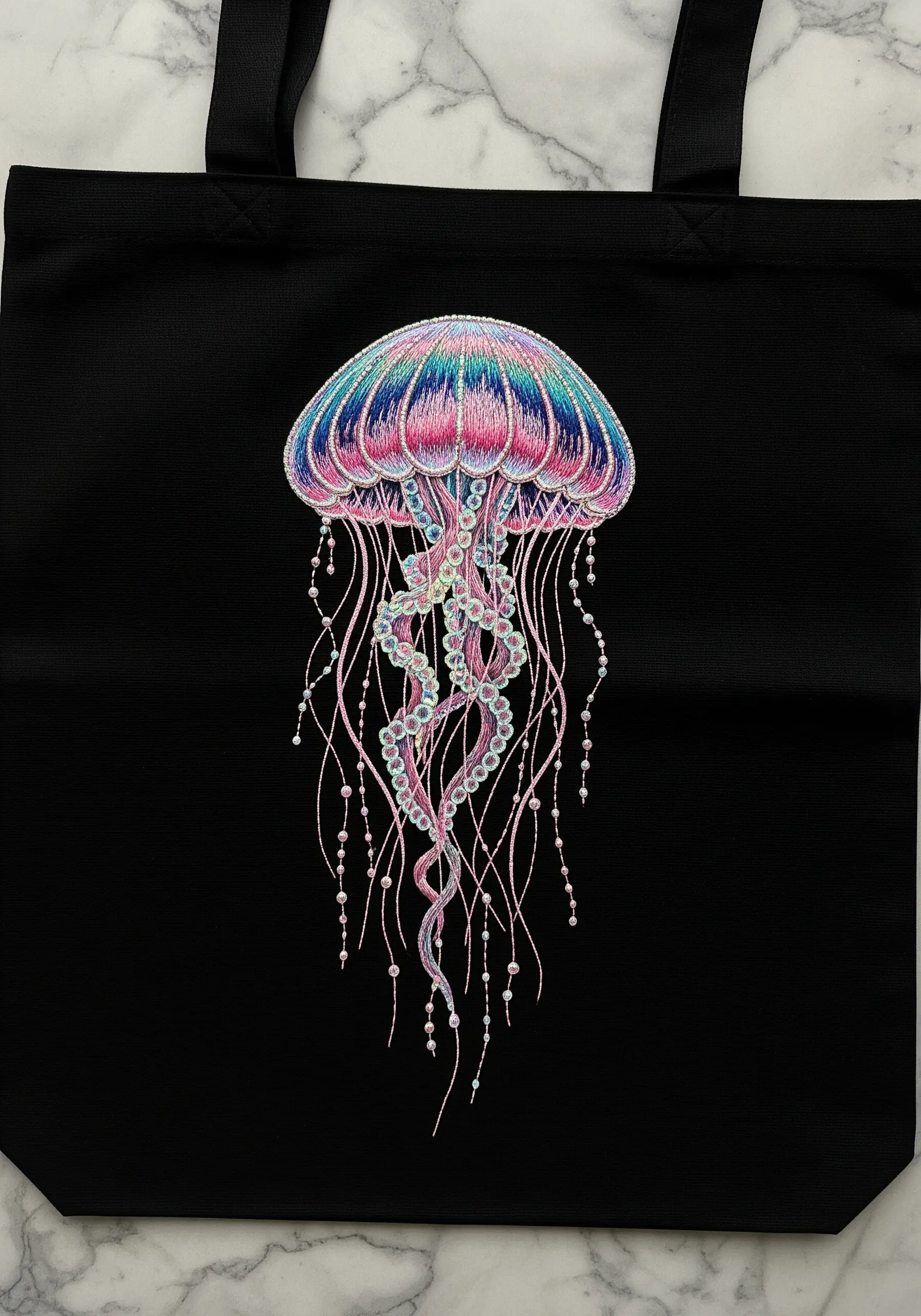 A vibrant, iridescent jellyfish embroidered with metallic threads and beads on a black tote bag.