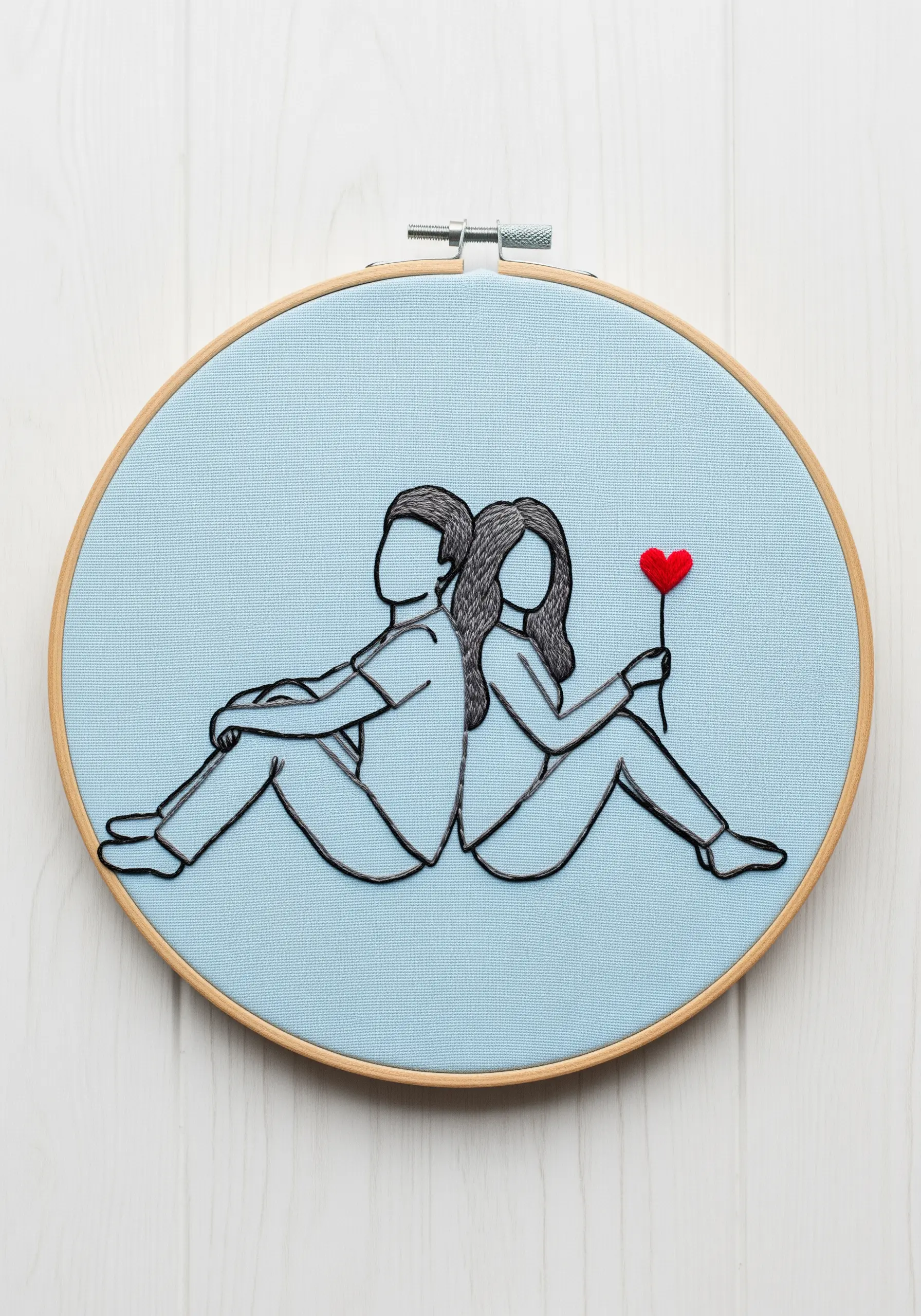 Line art embroidery of a couple sitting back-to-back with a single red satin-stitched heart.